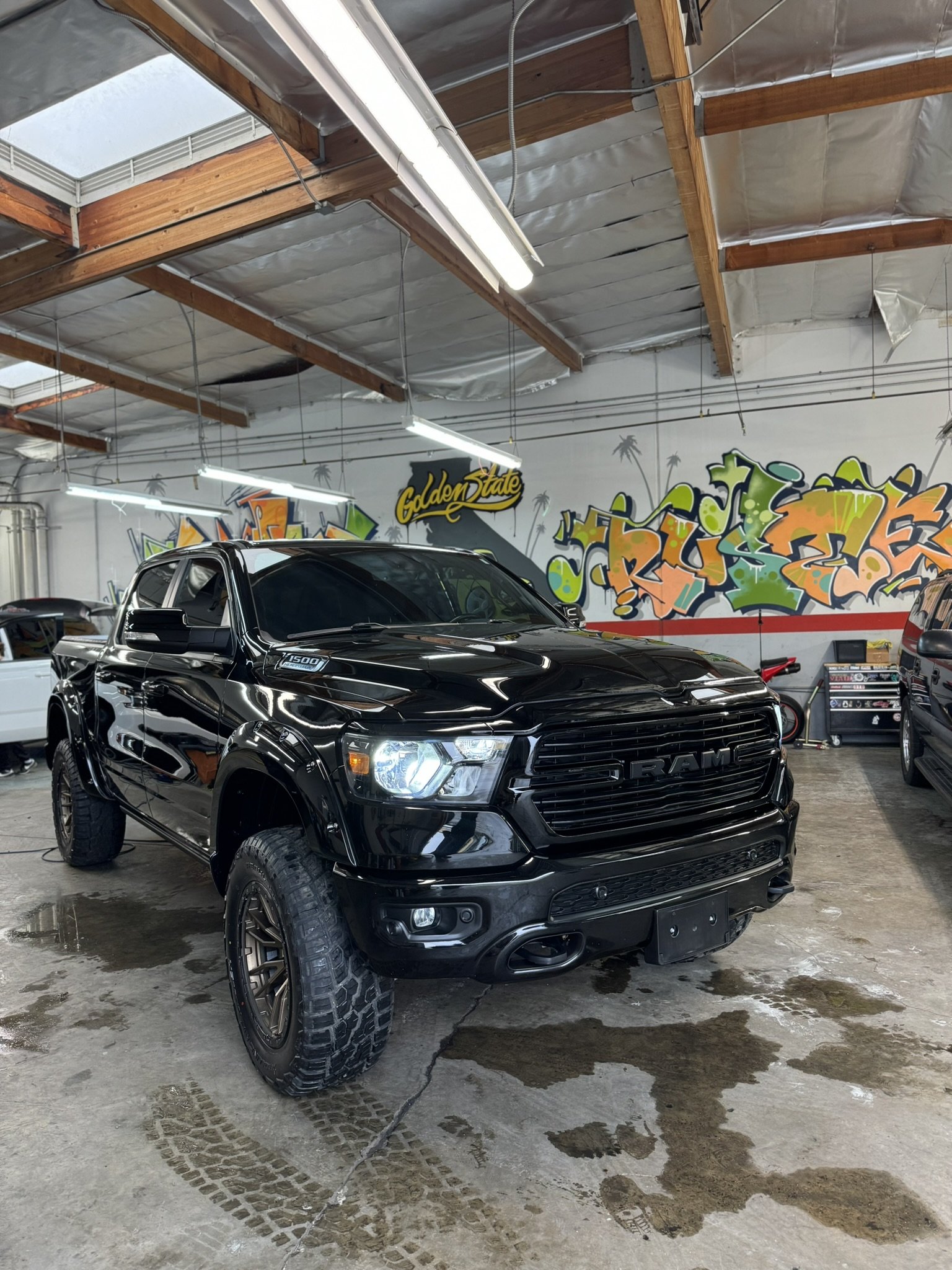 Black Ram truck parked inside a garage with graffiti on the walls and overhead fluorescent lighting.