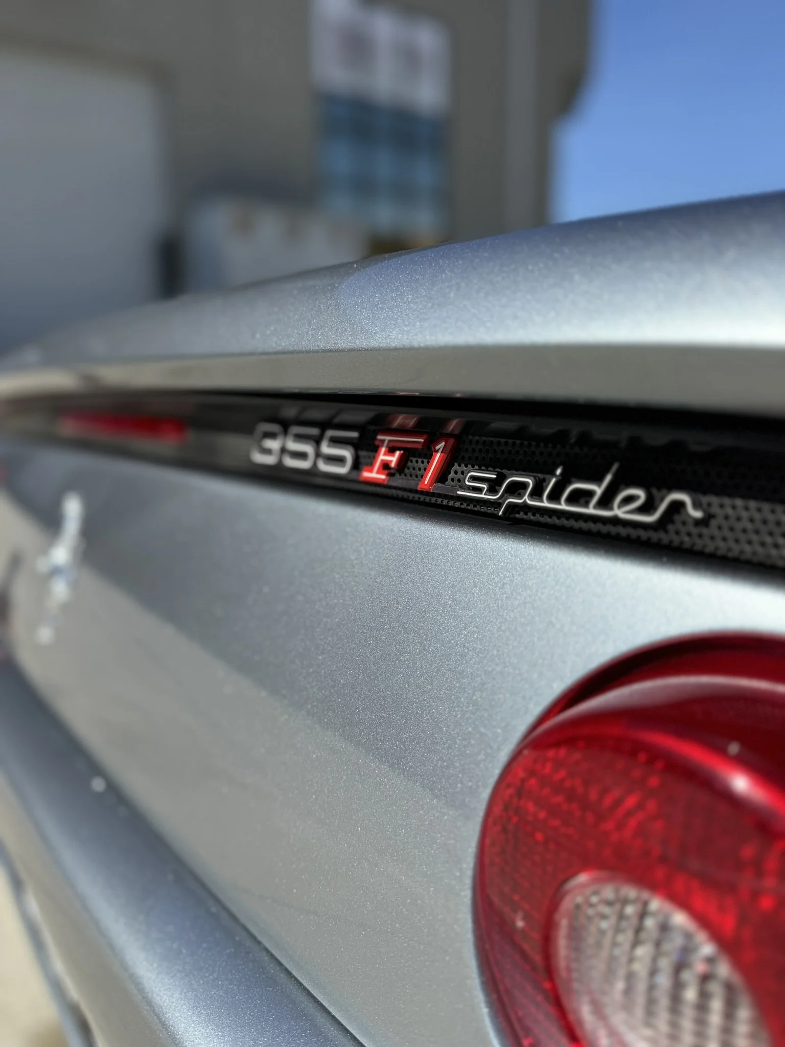 Close-up of a silver Ferrari 355 F1 Spider badge and rear light.