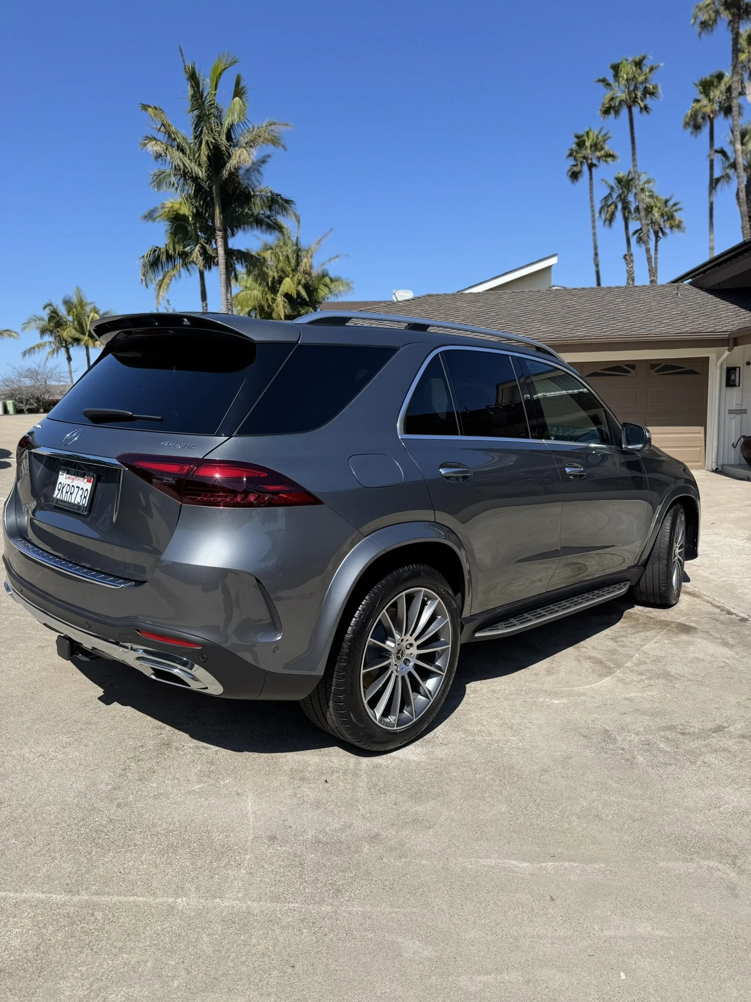 A gray SUV parked in a driveway with palm trees in the background on a sunny day.