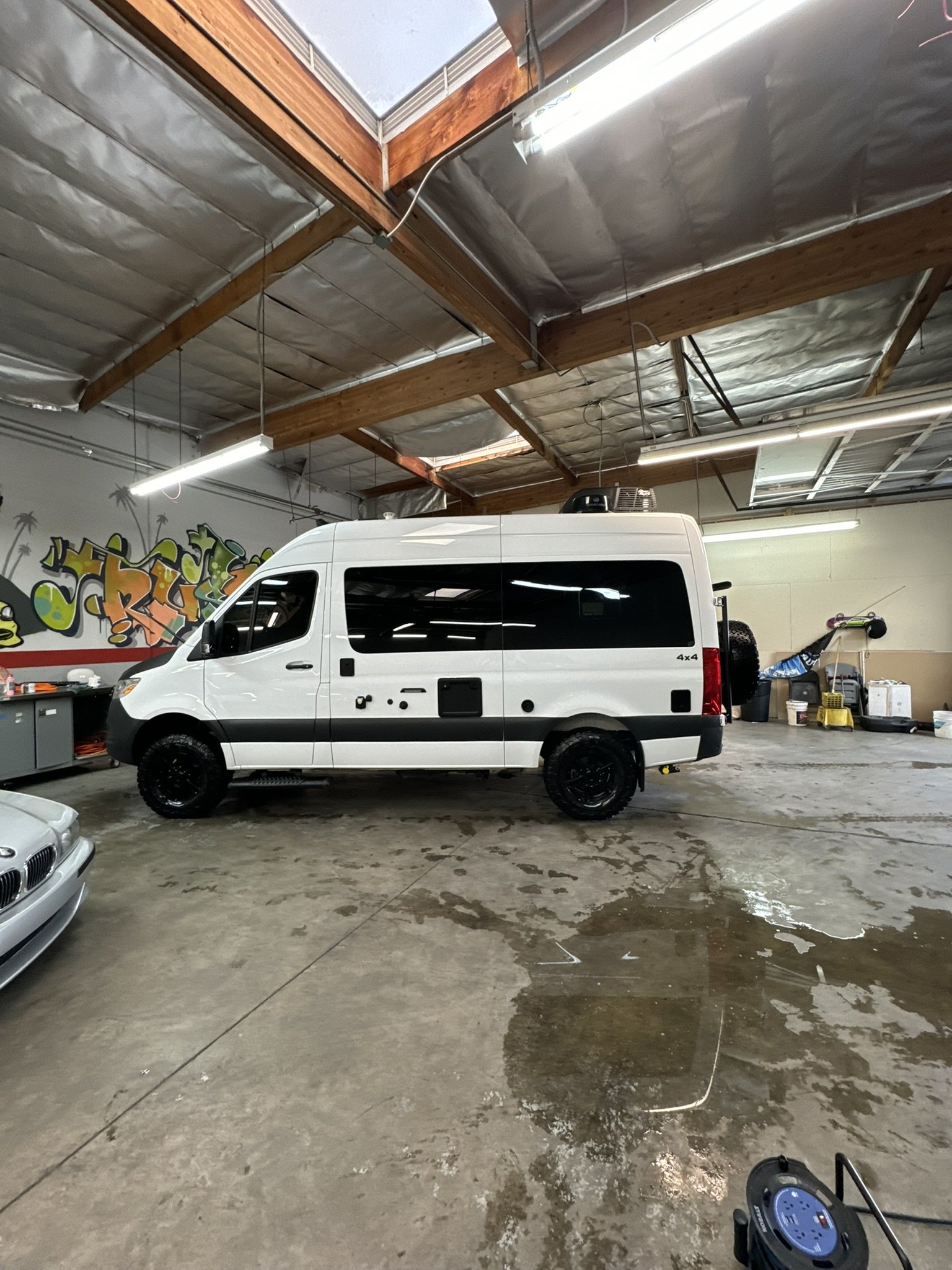 White camper van parked indoors with graffiti and industrial equipment.