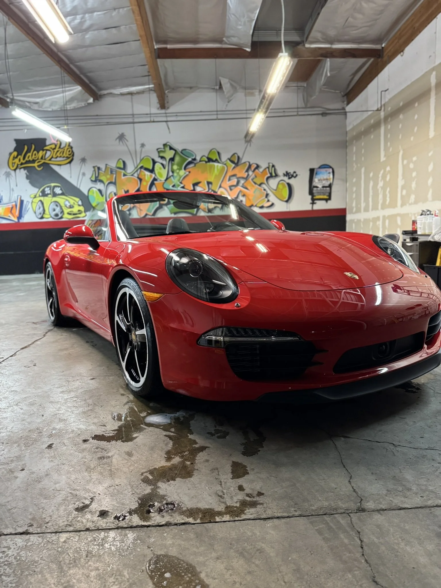 Red convertible sports car in a garage with graffiti art on the walls.