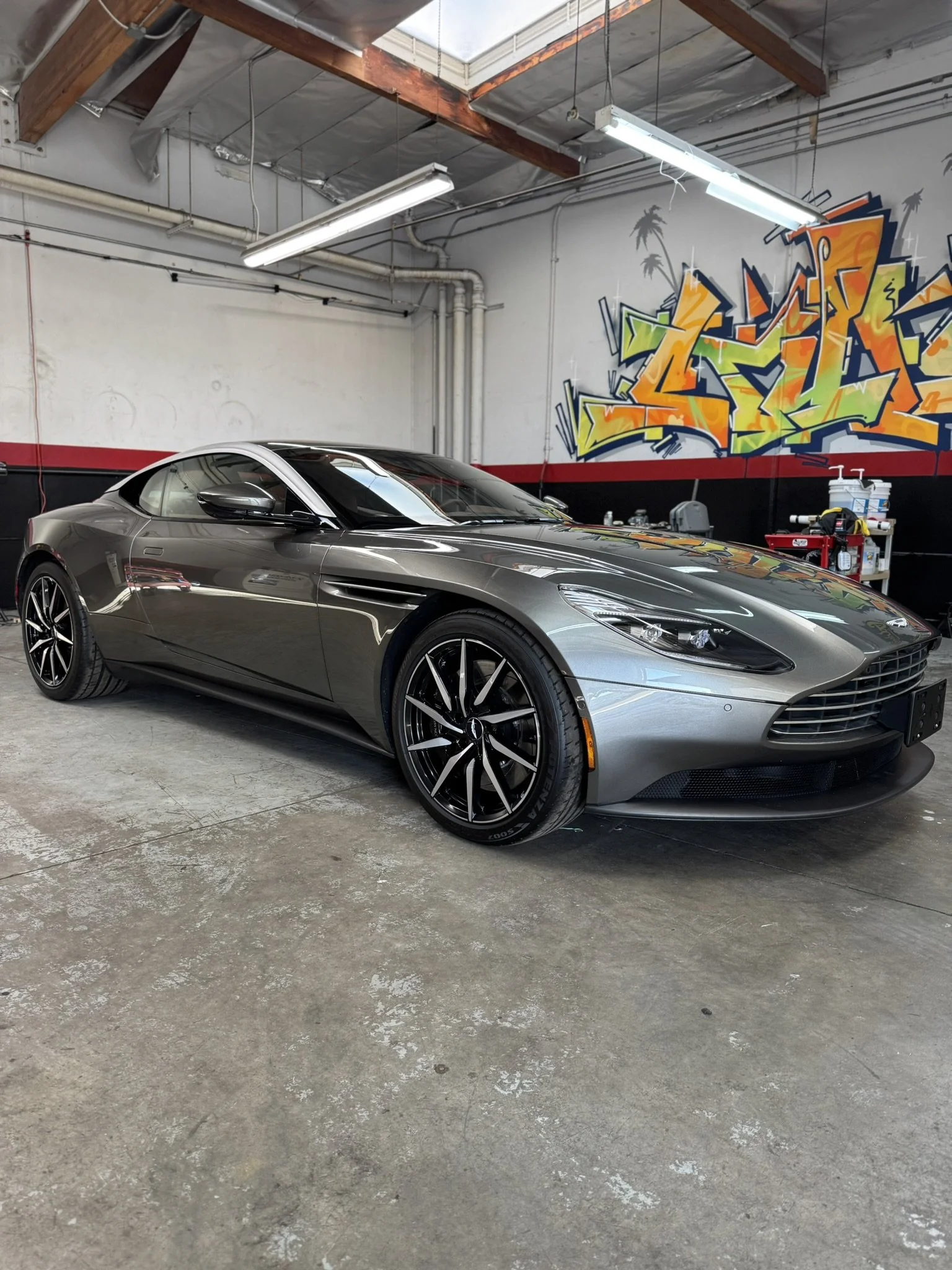 Luxury silver sports car in a garage with graffiti artwork on the wall.