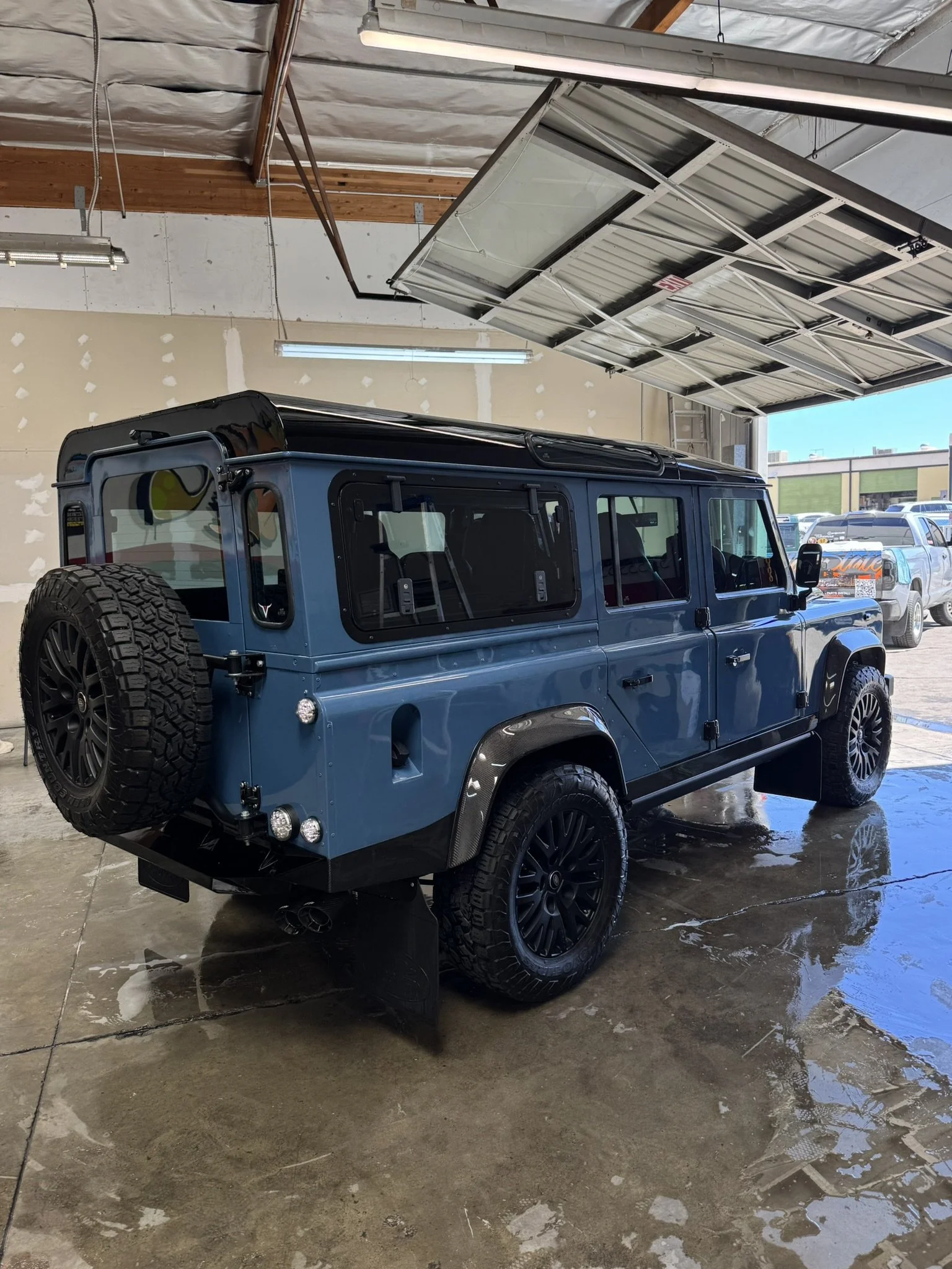 Blue SUV parked inside a garage with an open overhead door, spare tire attached to the rear, and glossy black wheels.