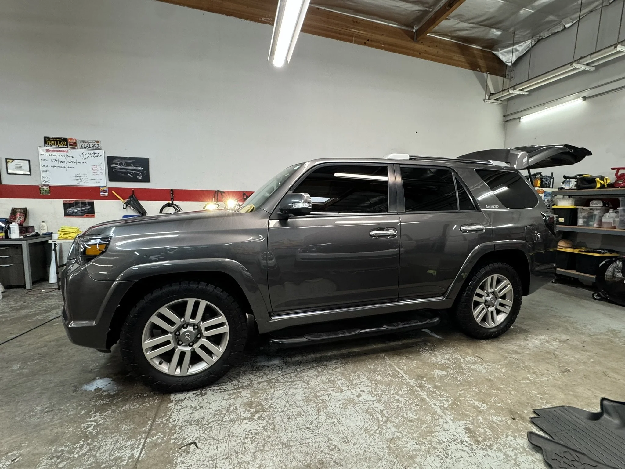 Gray SUV parked inside a garage with open trunk, surrounded by automotive tools and equipment. Interior features visible through open windows.