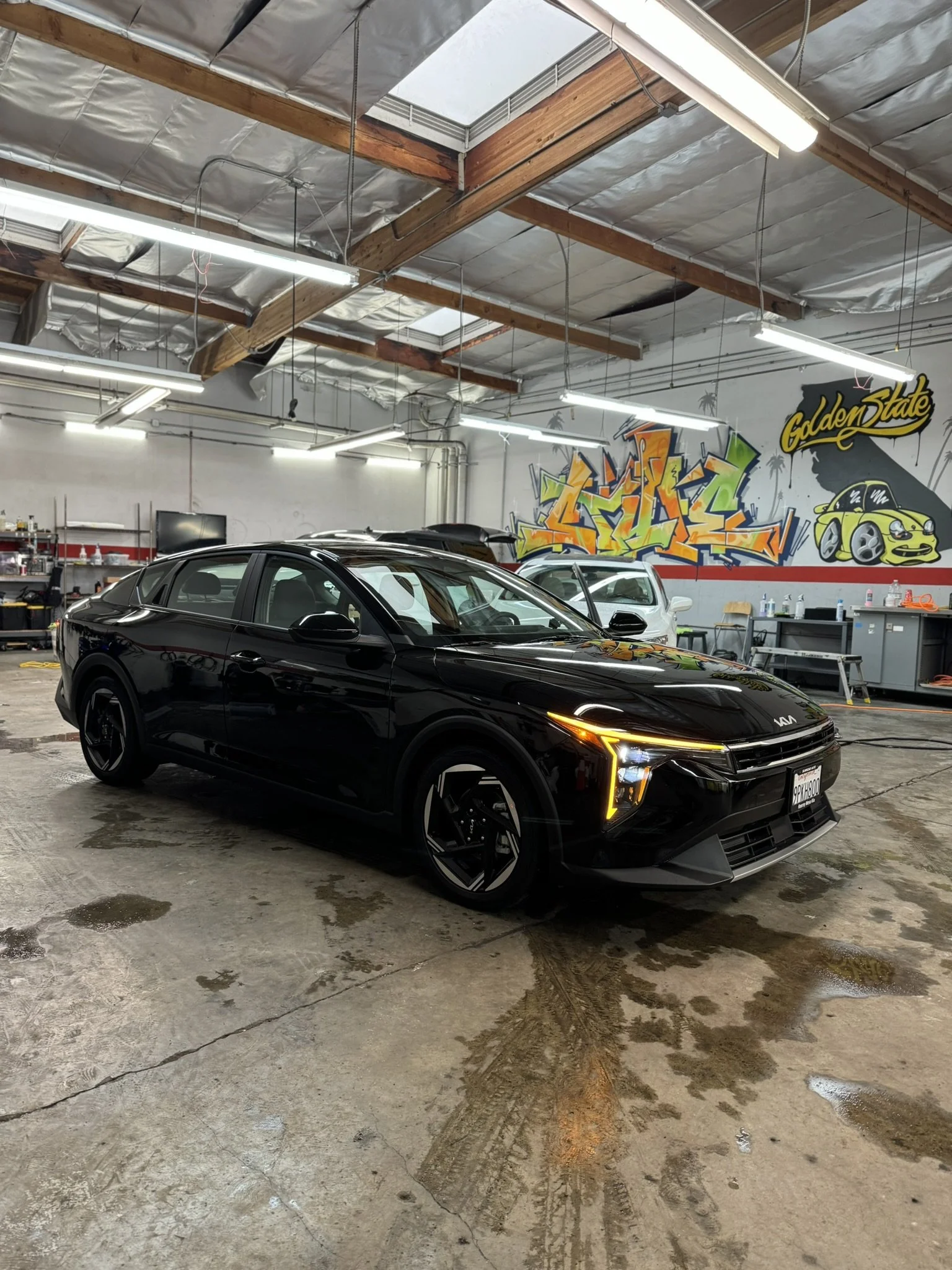 Black Kia electric car in a garage with graffiti on the wall, concrete floor, and fluorescent lighting.