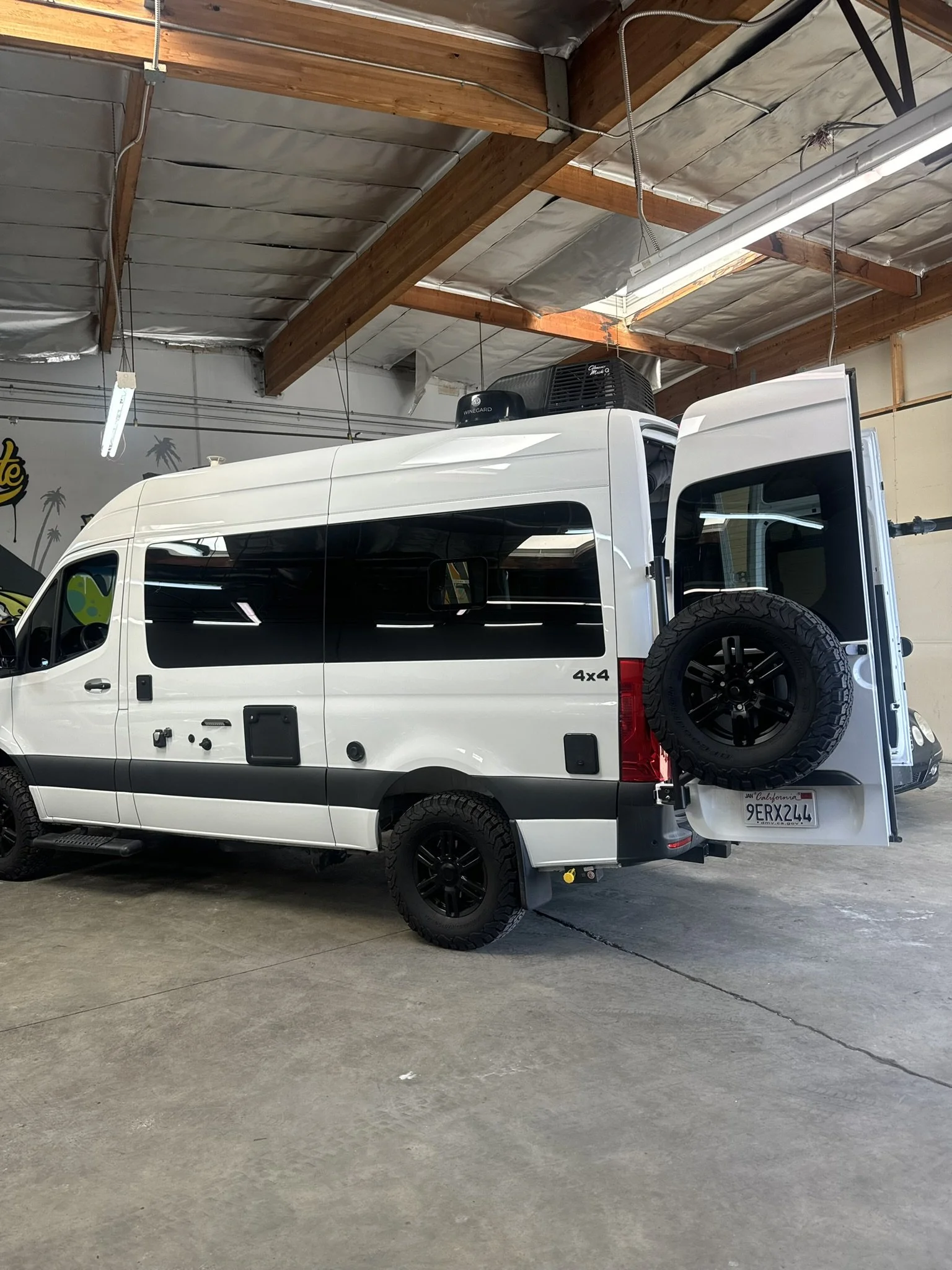 White 4x4 van parked inside a garage with high ceiling and wooden beams.