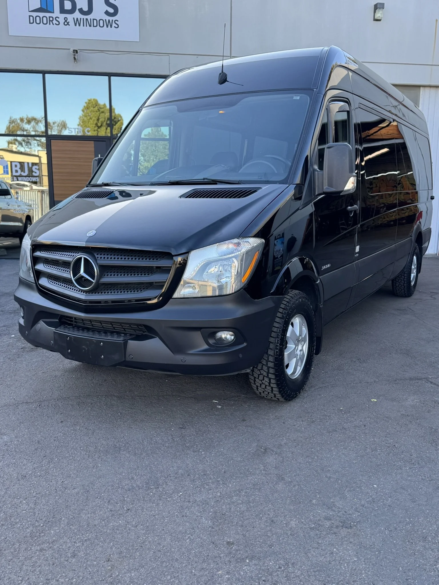 Black Mercedes-Benz Sprinter van parked outside BJ's Doors & Windows.