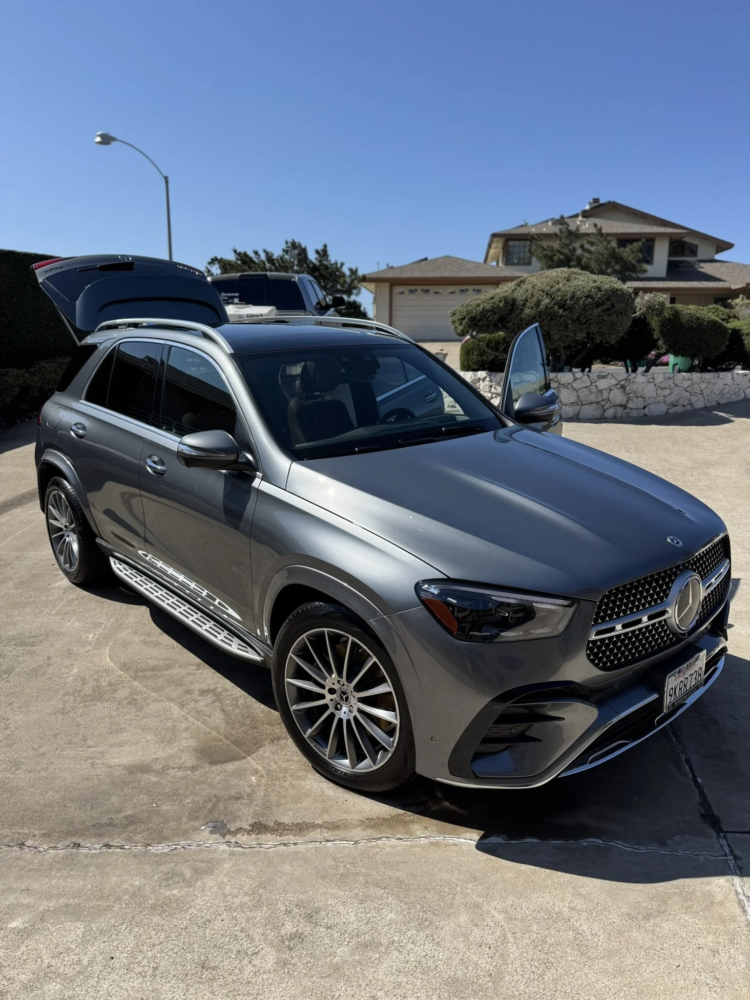 Silver Mercedes-Benz SUV parked on a driveway, with the driver's door and trunk open, residential house in the background.