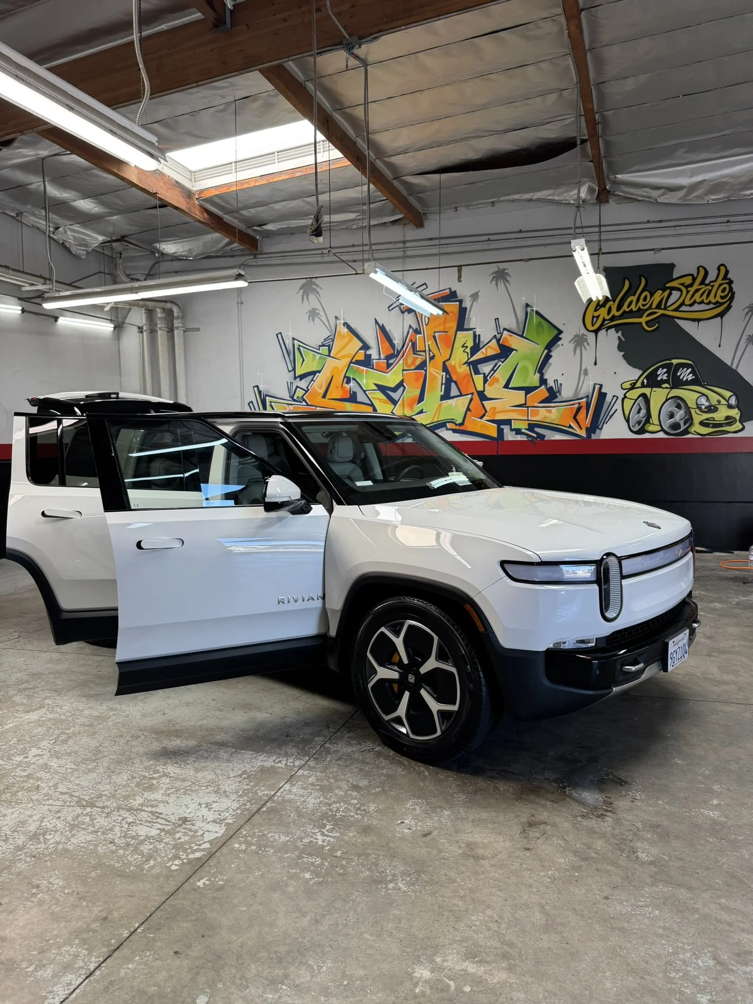 White Rivian R1T electric truck in a garage with graffiti on the wall.