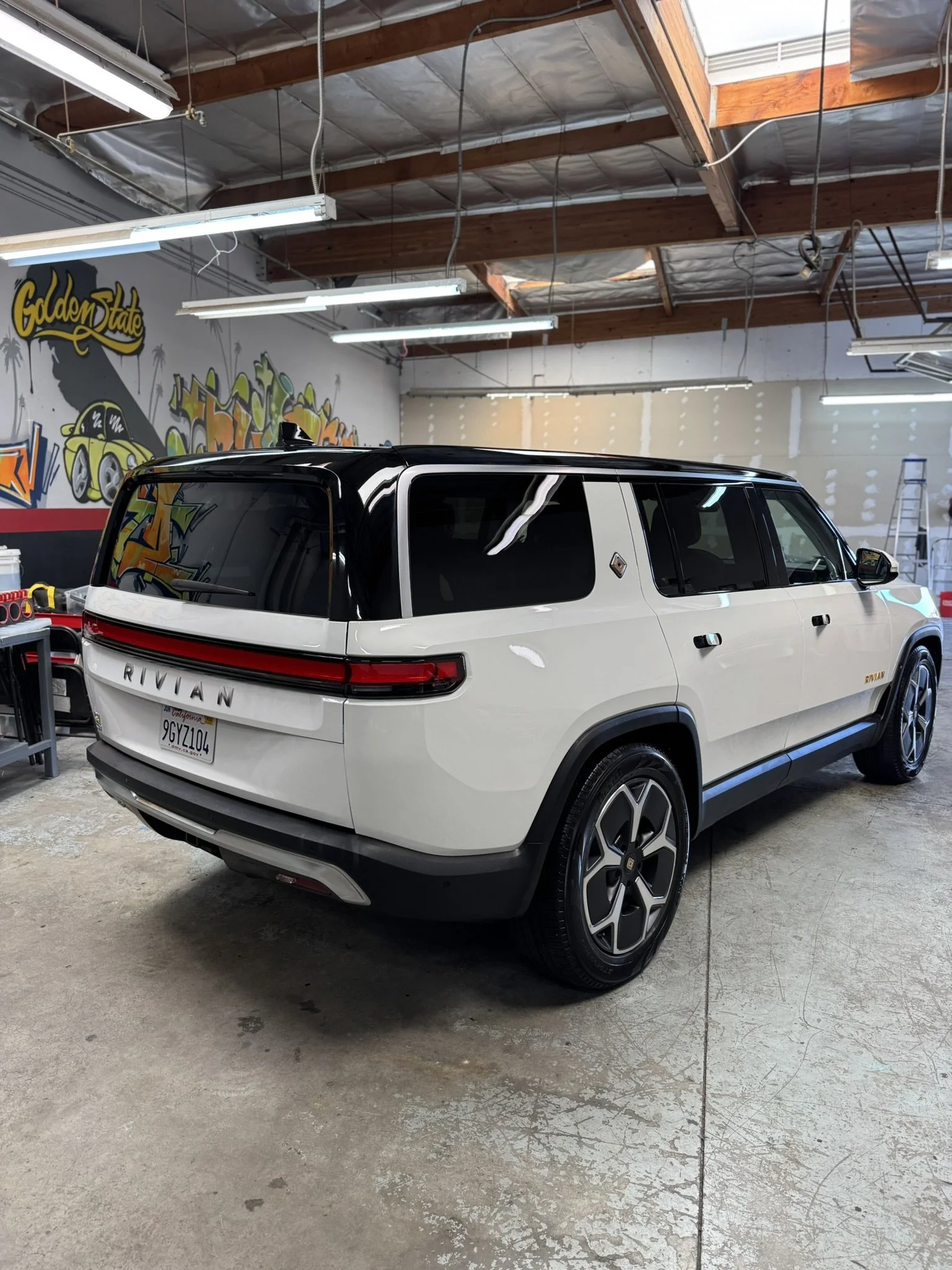 White Rivian SUV parked inside a garage with graffiti-covered walls.