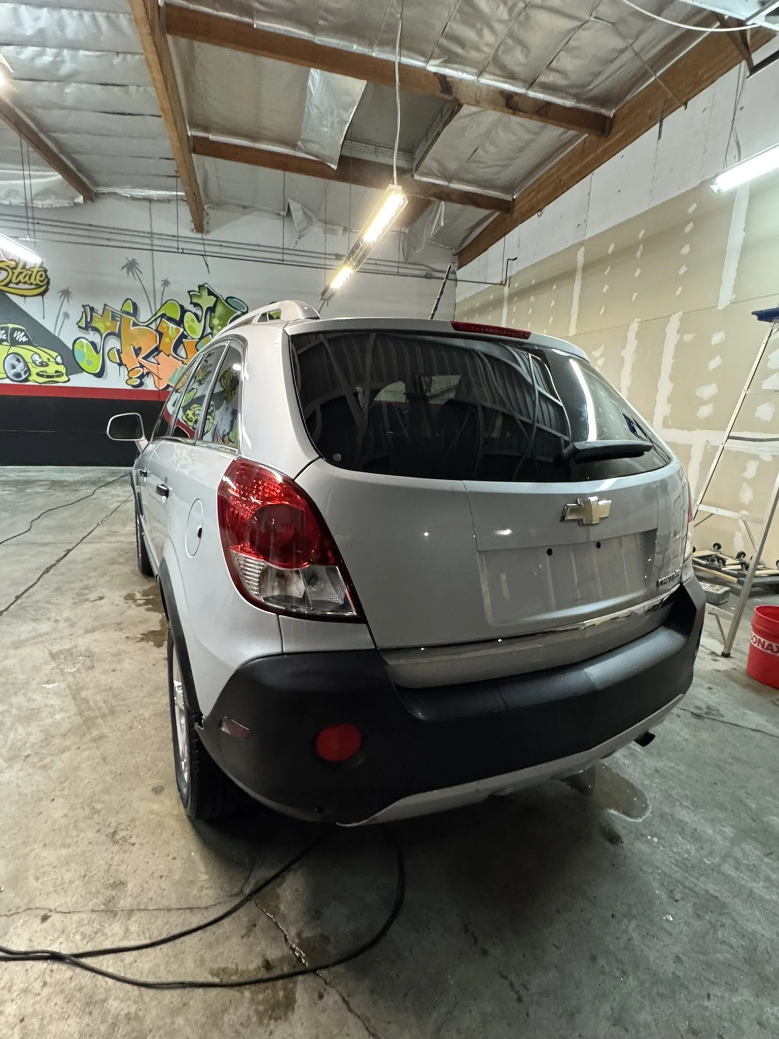 Rear view of a white crossover SUV parked in an indoor garage with graffiti art on the wall.