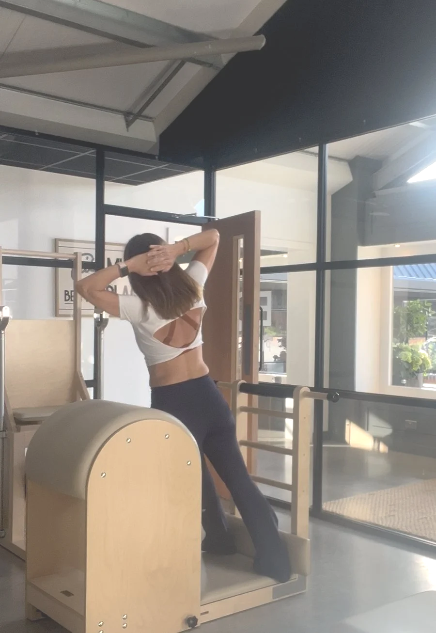 A woman stretching in a modern indoor space with large windows, wooden and metal furniture, and natural light.