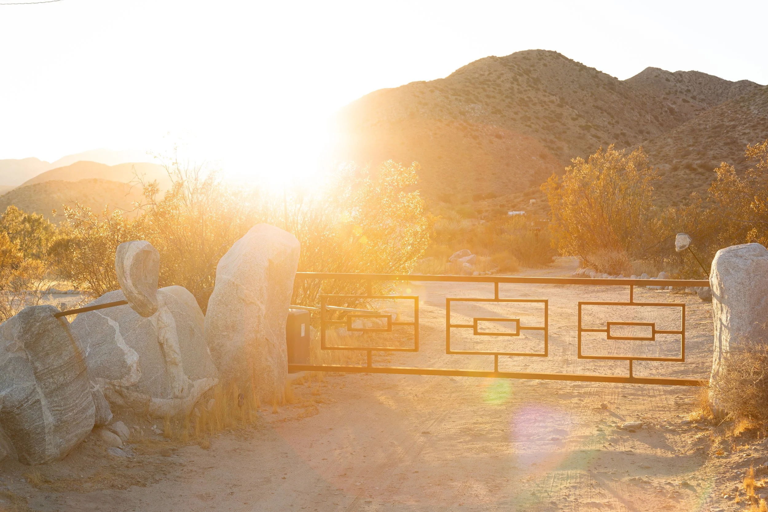 Sunlit gate in desert landscape with hills in the background.