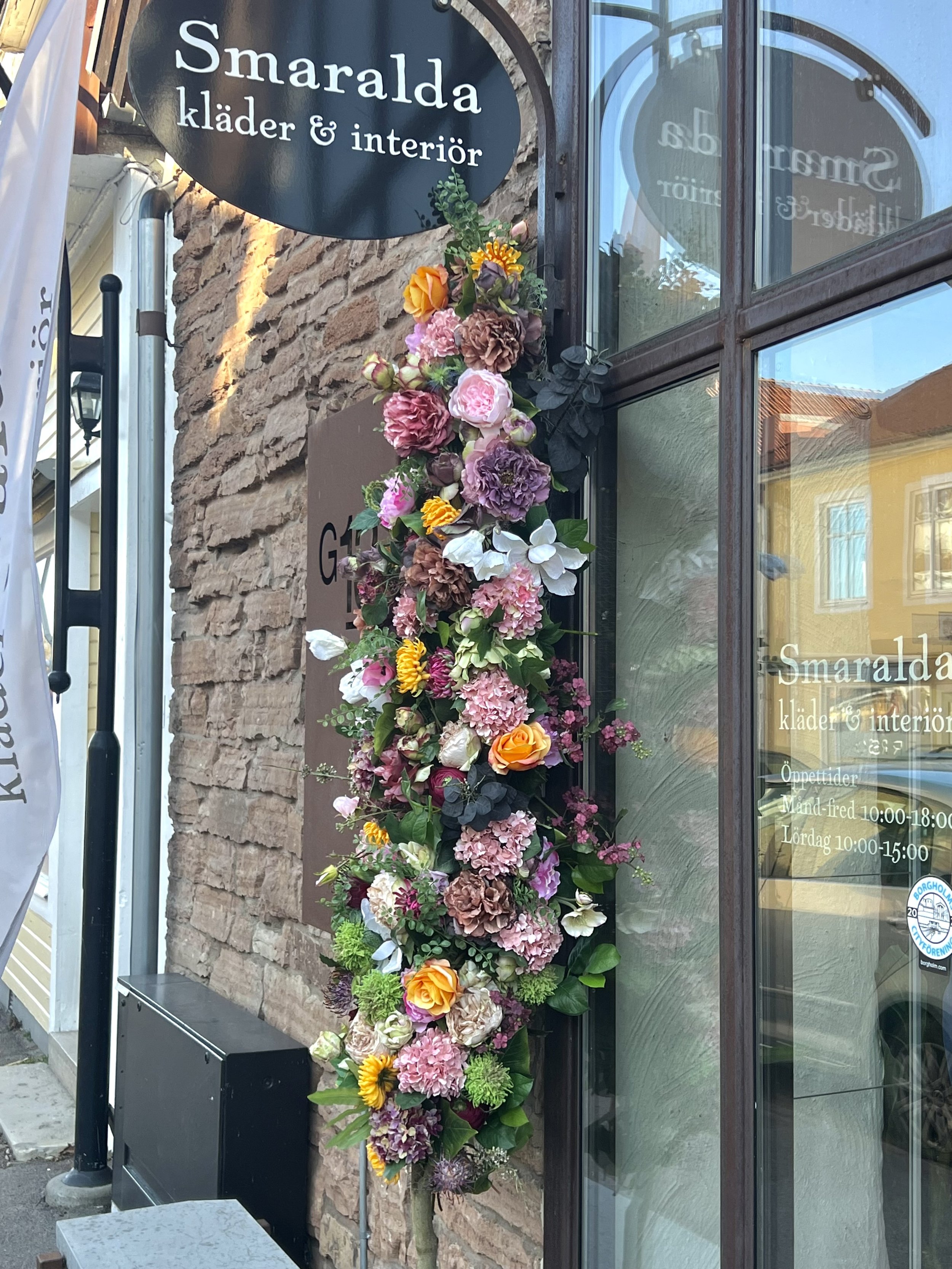 Färgstarka blommor som dekoration utanför en butik med skylt för Smaralda kläder & interiör.