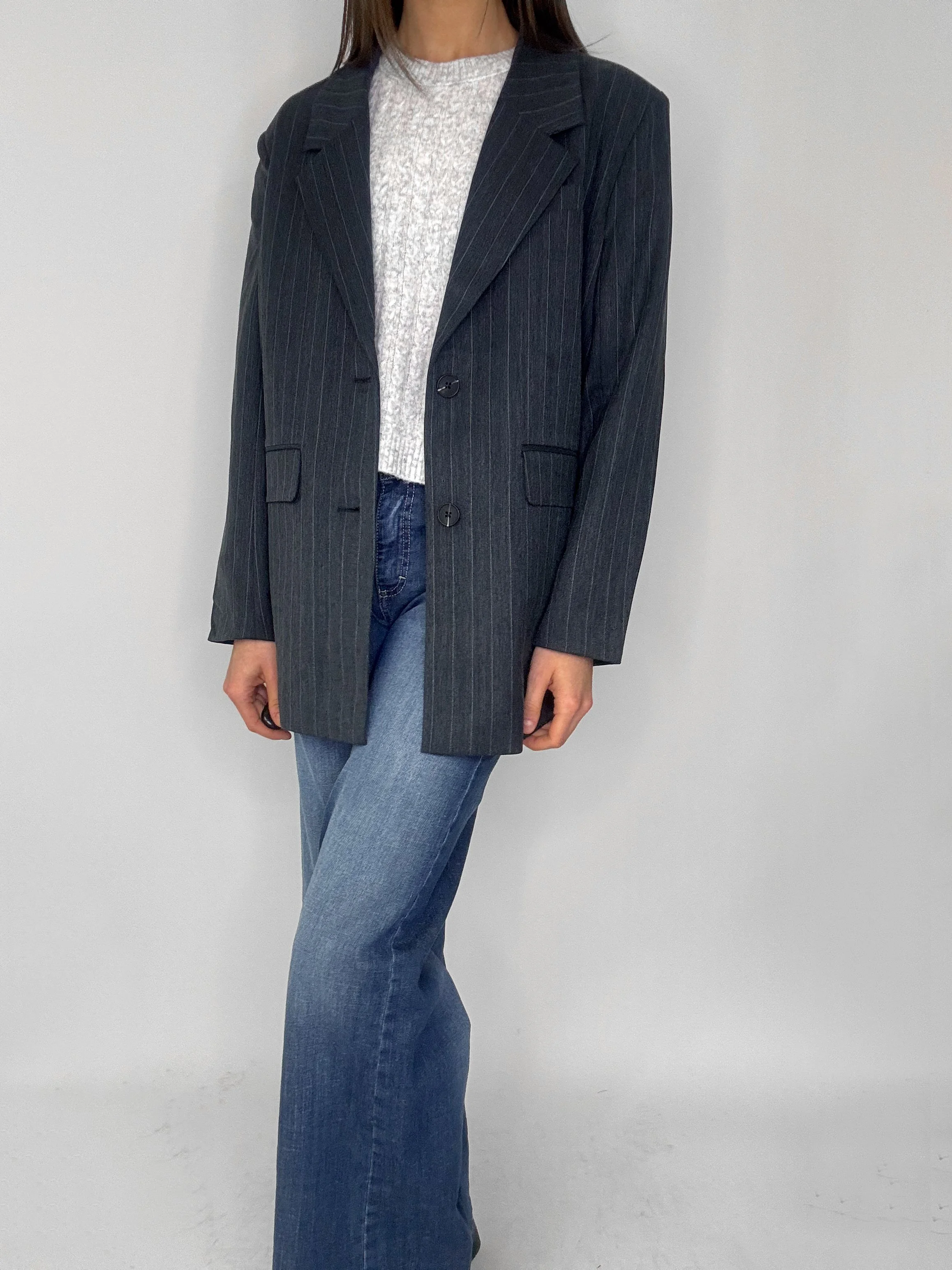 Tre stickade tröjor i vita, rosa och gråa, hängande på en metallställning.