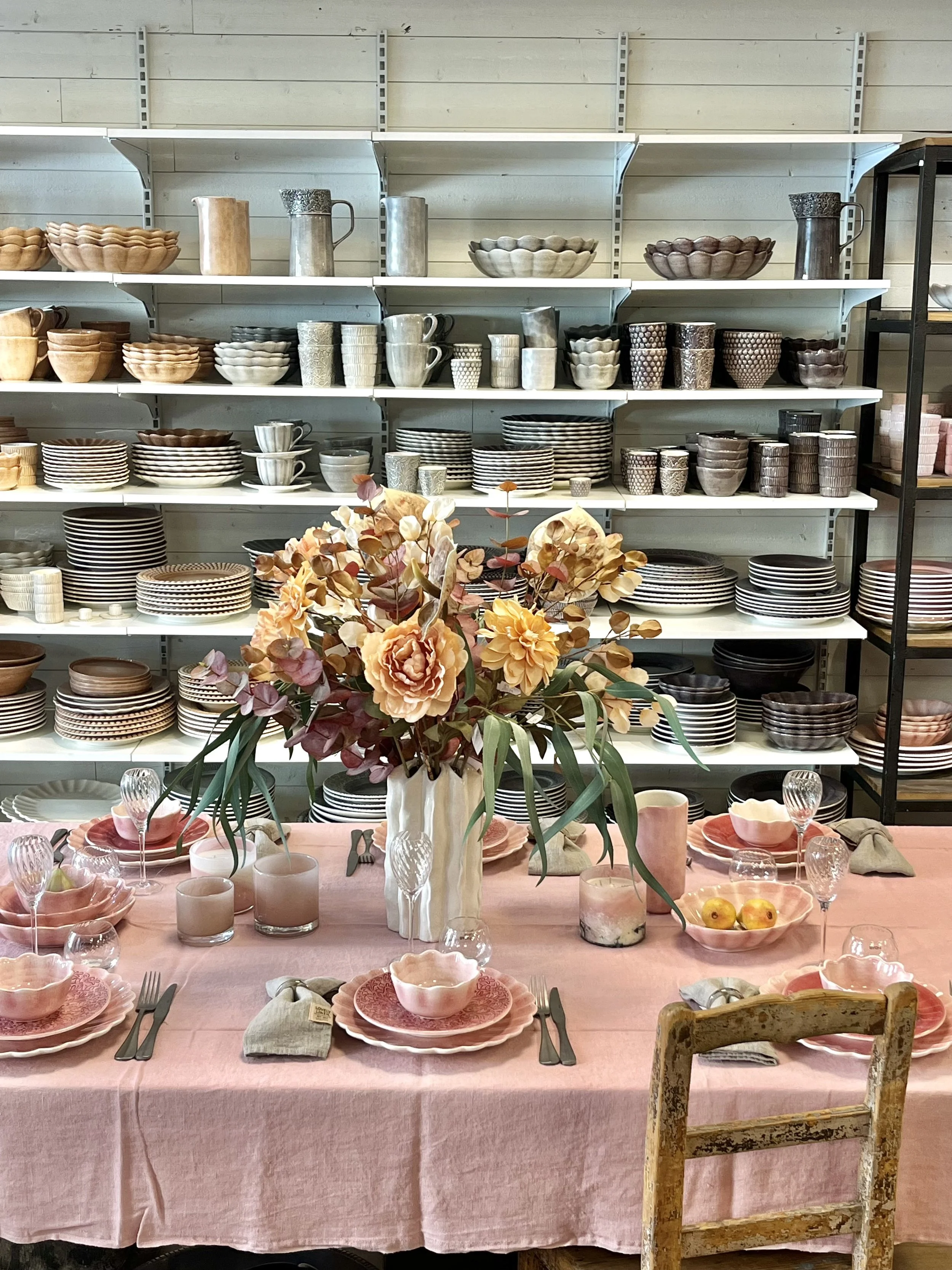 En tallrik med blå och orange blommönster, en skål och guldfärgade bestick på en rosa duk.