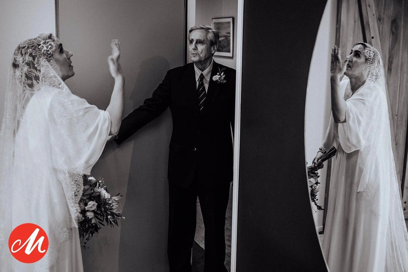 Zwei Frauen im Hochzeitskleid und ein älterer Mann in Anzug stehen vor einem Spiegel, eine Frau zeigt auf sich und die andere blickt nach oben, Szene bei einer Hochzeitsvorbereitung.