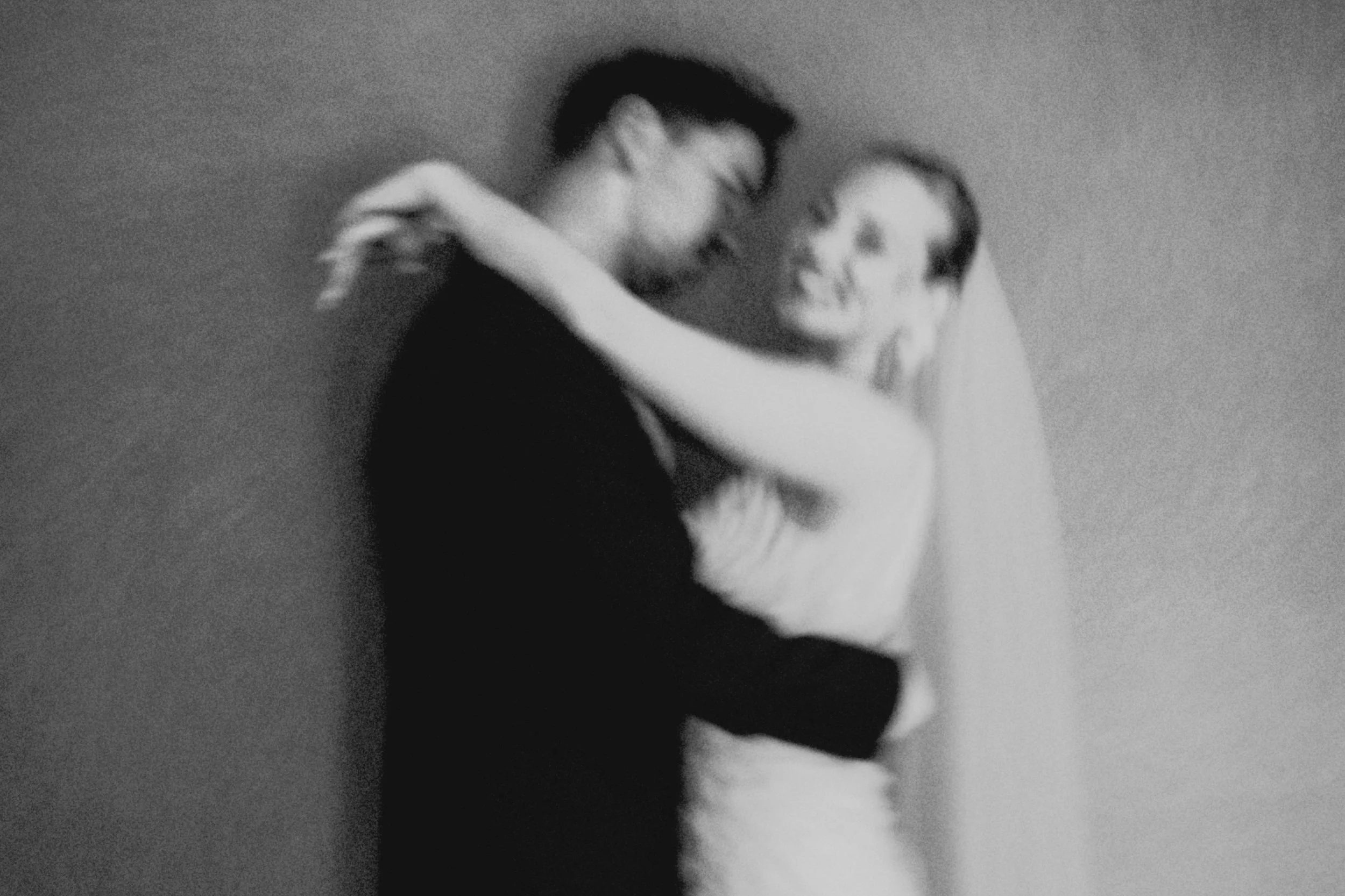 Ein schwarz-weiß-Foto von einem Mann und einer Frau, die sich umarmen, lächeln und nah beieinander stehen, die Freude und Nähe ausdrücken.