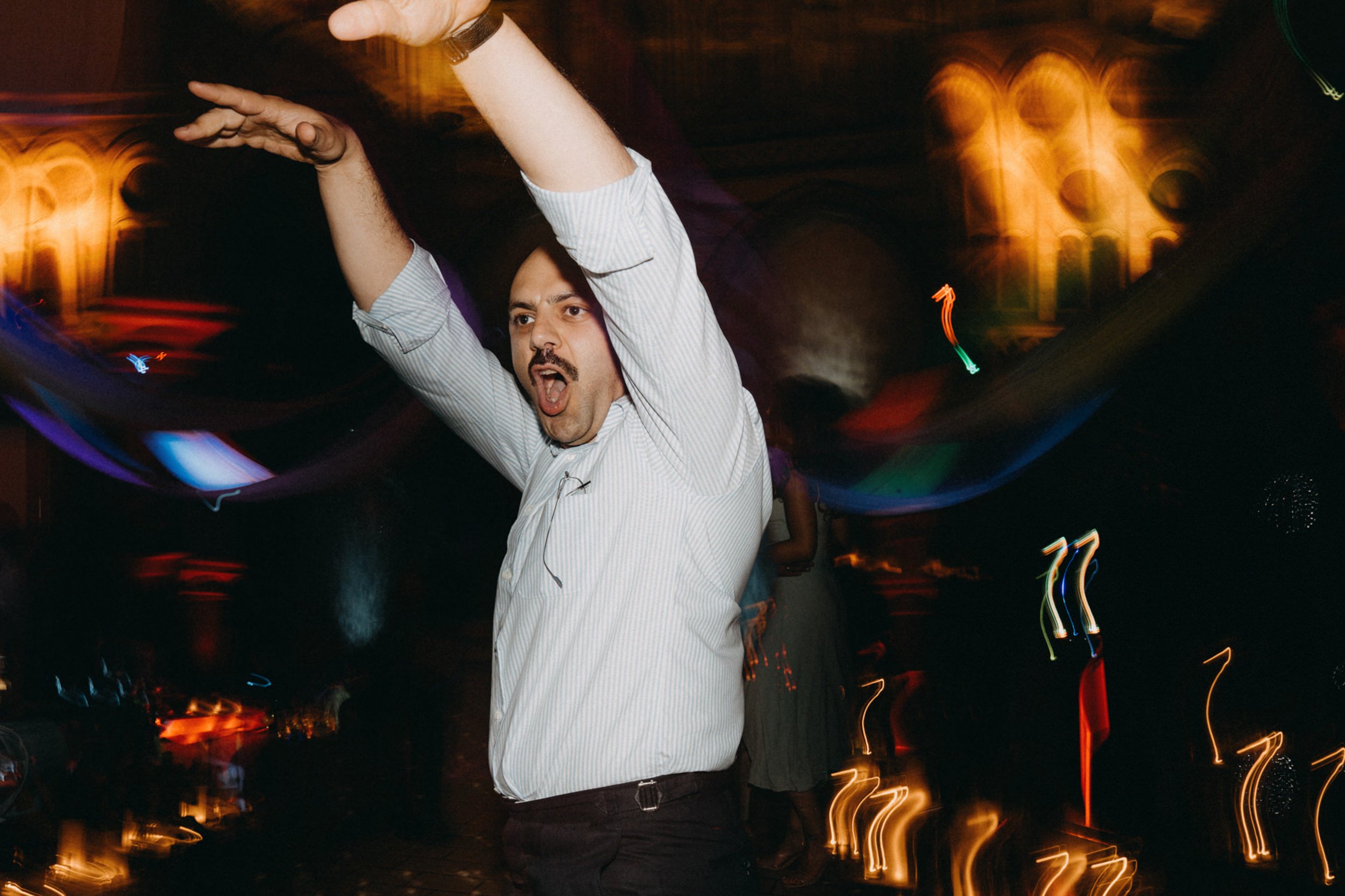 Ein Mann mit offenem Mund, der bei einer Party tanzt, bei Nacht mit bunten Lichtern.
