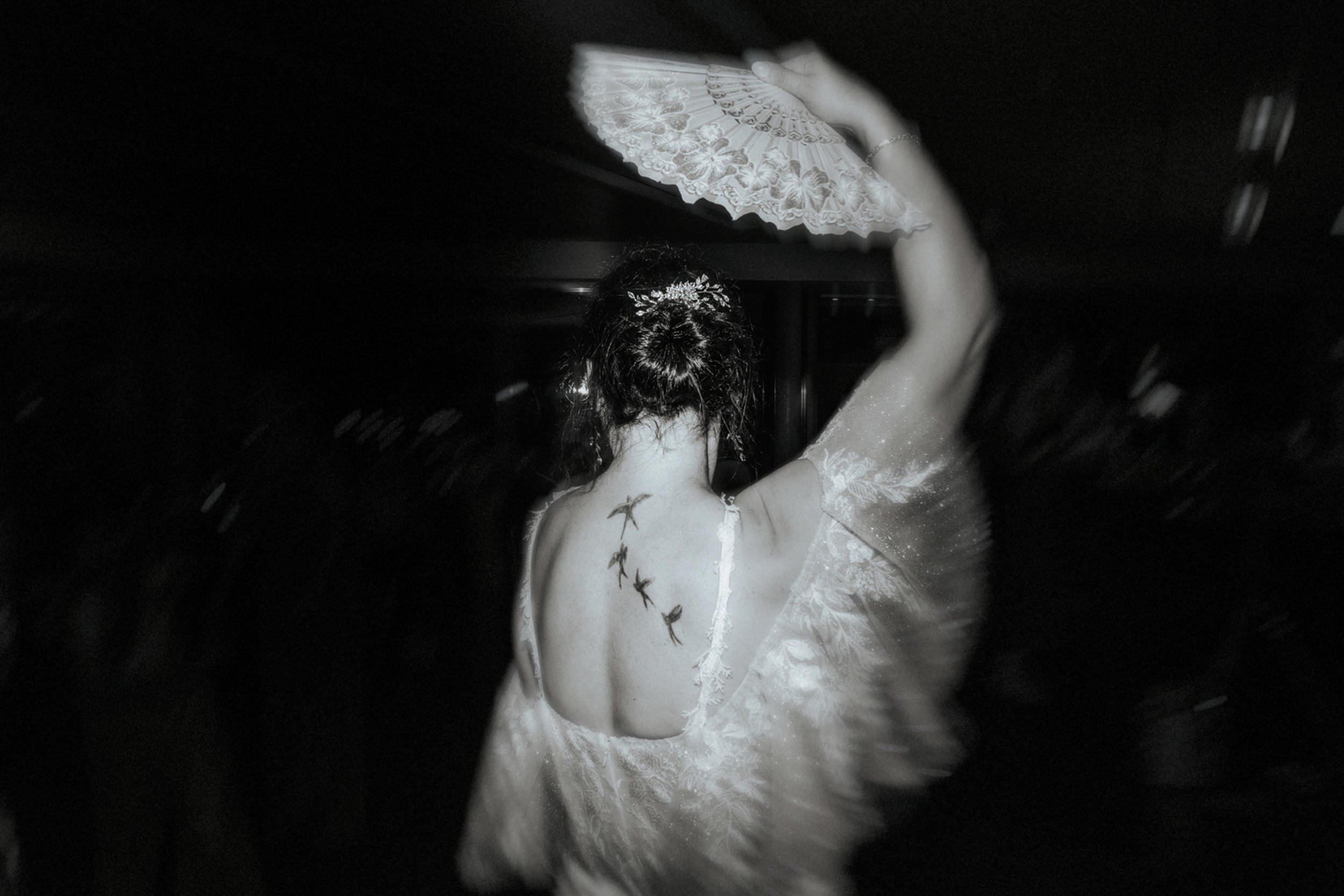 Frau in einem weißen Brautkleid, die einen Handfächer hält, fotografiert von hinten.