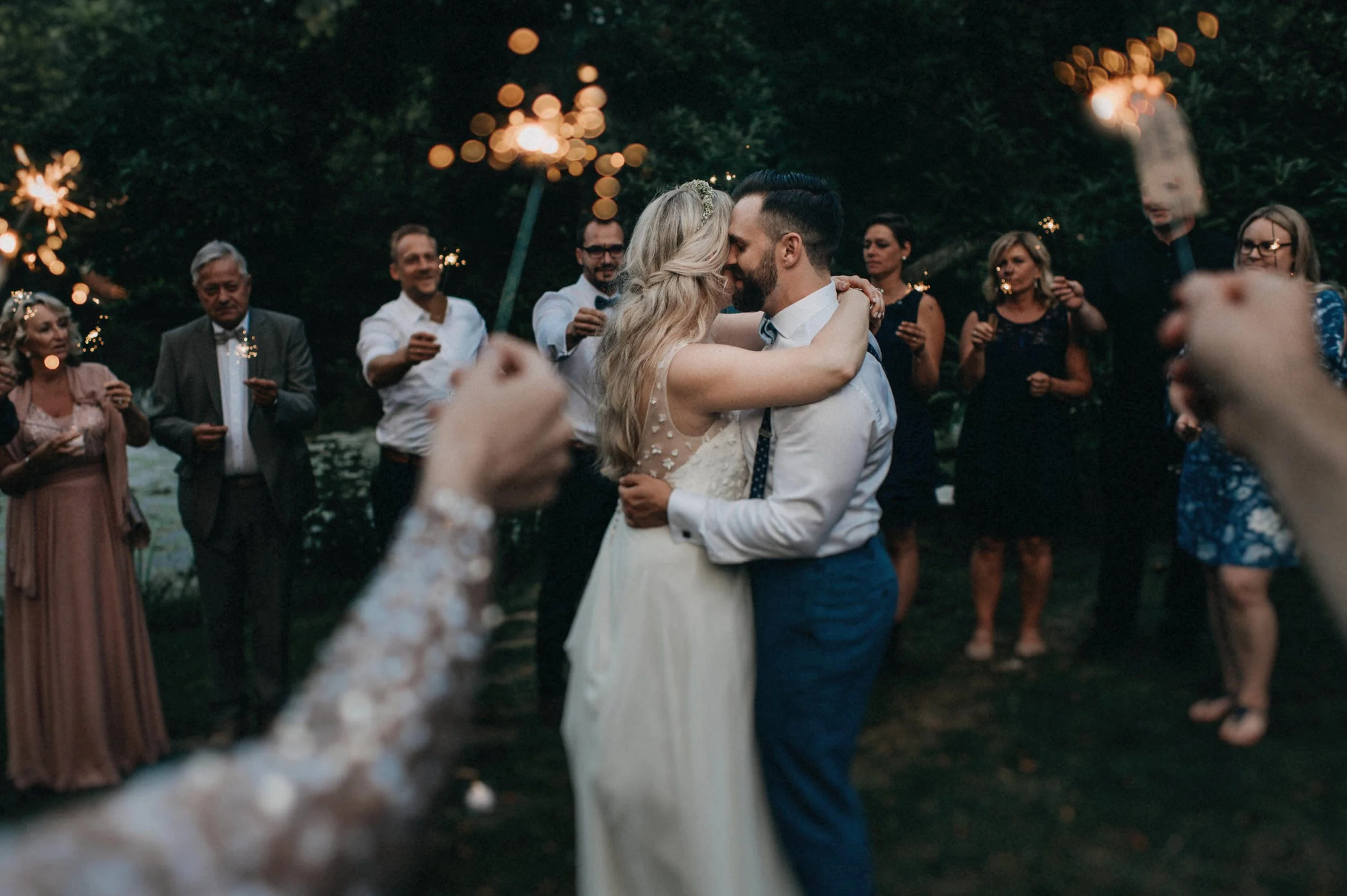 Ein Brautpaar tanzt bei einer Hochzeit im Freien, umgeben von Gästen, bei Nacht mit Scheinwerfern im Hintergrund.