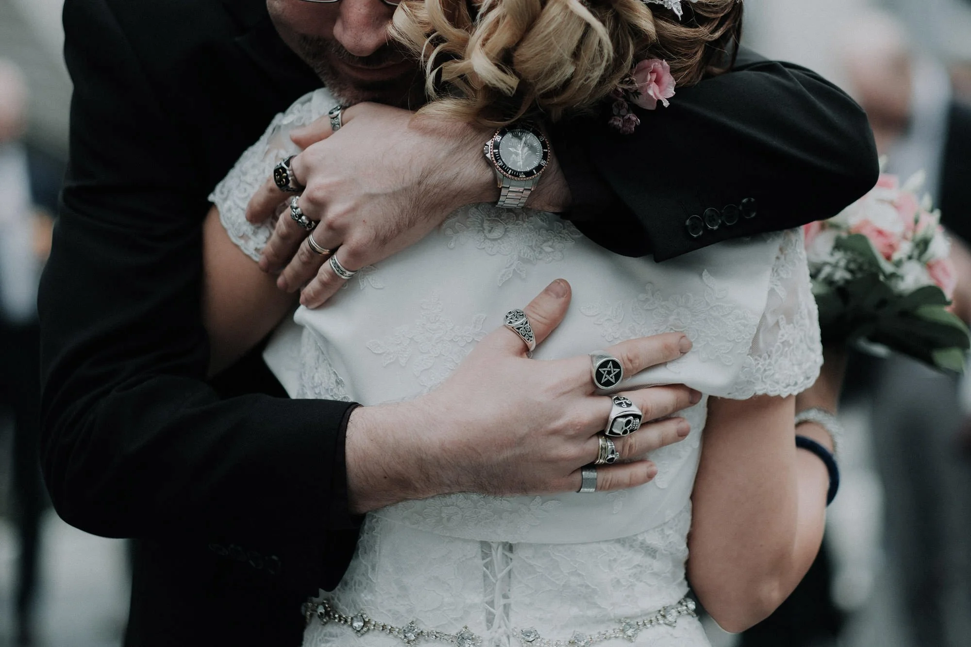 Nahaufnahme eines Mannes und einer Frau, die sich umarmen, Kleidung im schwarzen und weißen Hochzeitsstil, viele Schmuckstücke, Armband, Ringe, auf ihrer Kleidung und Hand, zweiteilig, emotionaler Moment
