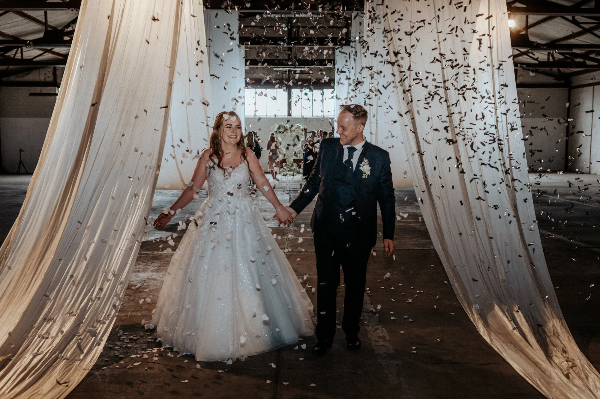 Ein Brautpaar hält Händchen, geht durch eine Feier an einem Hochzeitstag, und wird von Konfetti umgeben.