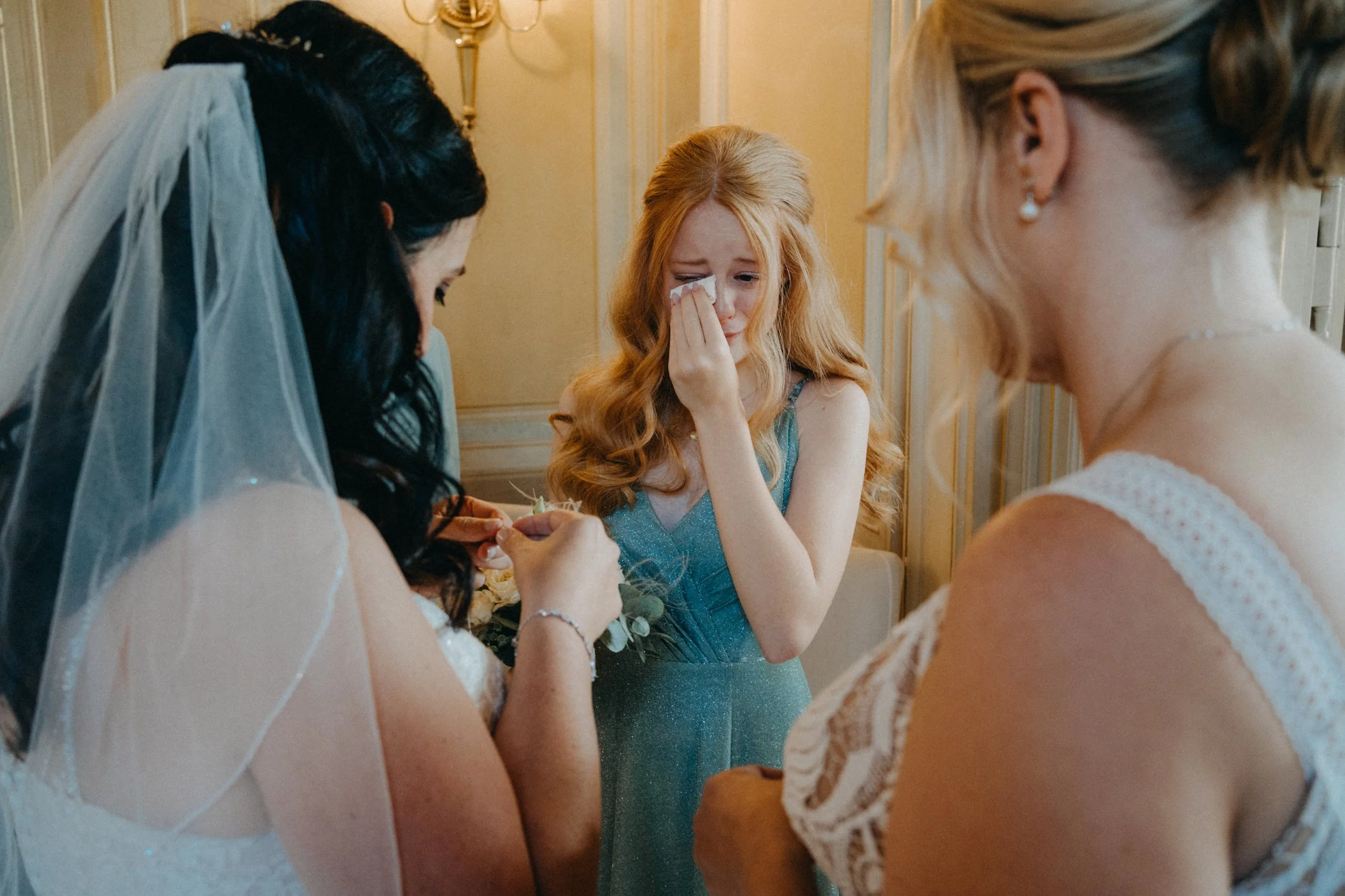 Eine junge Frau bei einer emotionalen Zeremonie, möglicherweise bei einer Hochzeit, weint und wird von drei Frauen umgeben.