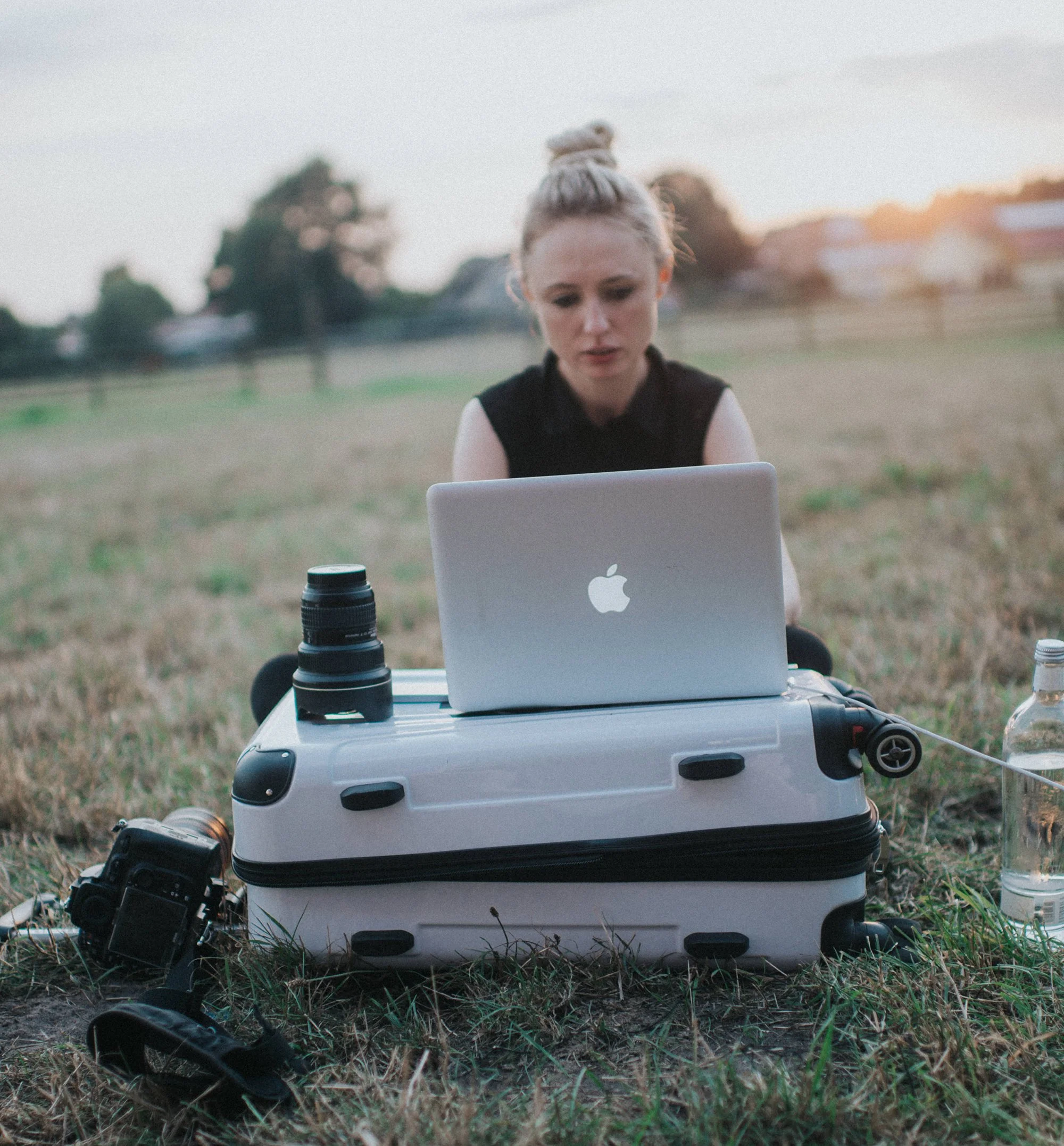 Fotografie eines Drohnen-Controllers, einer Kamera und eines Laptops, die auf einem weißen Koffer im Freien auf einem Feld liegen, während die Sonne im Hintergrund untergeht.