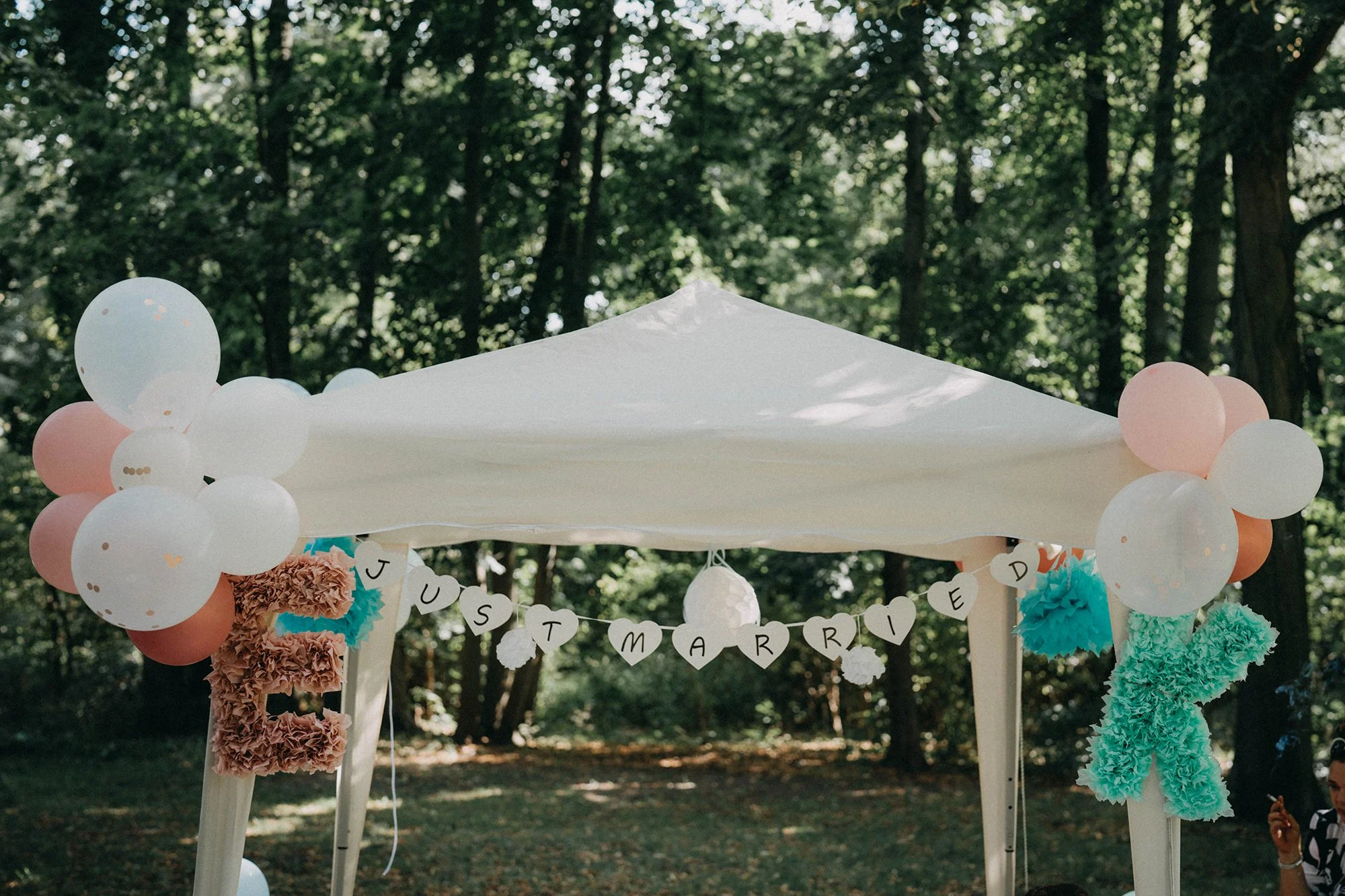 Hochzeitsszene im Freien mit Dekorationen und Ballons, eine Girlande mit Buchstaben spricht 'JUST MARRIED'.