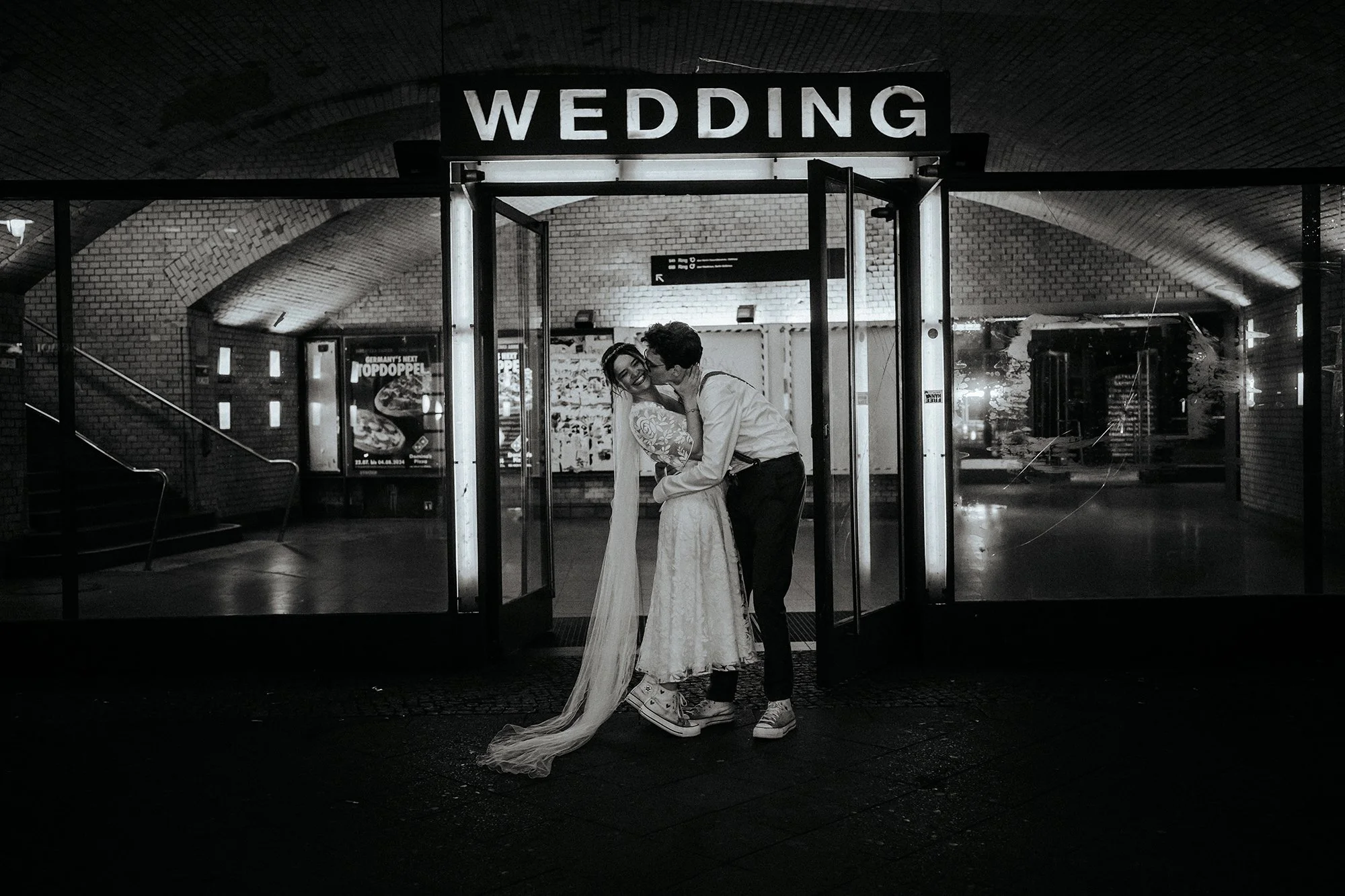 Ein Brautpaar in einem Tunnel vor einem Schilder mit dem Wort 'WEDDING', das sich ans Licht leuchtet, beim Verabschieden nach einer Hochzeit.
