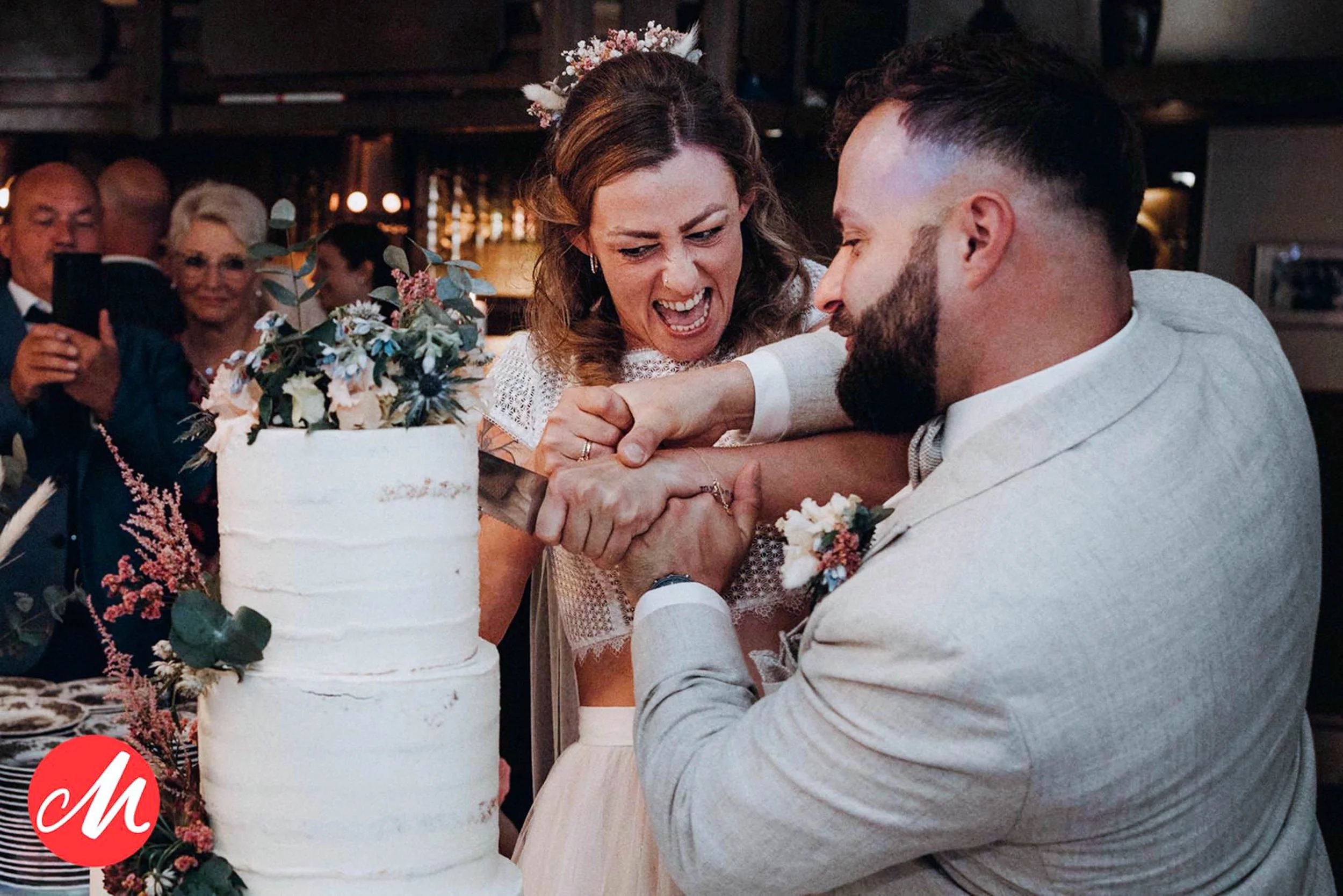 Ein Brautpaar feiert die Hochzeit, der Moment des Anschneidens der Hochzeitstorte bei einer eleganten Feier im Indoor-Bereich.