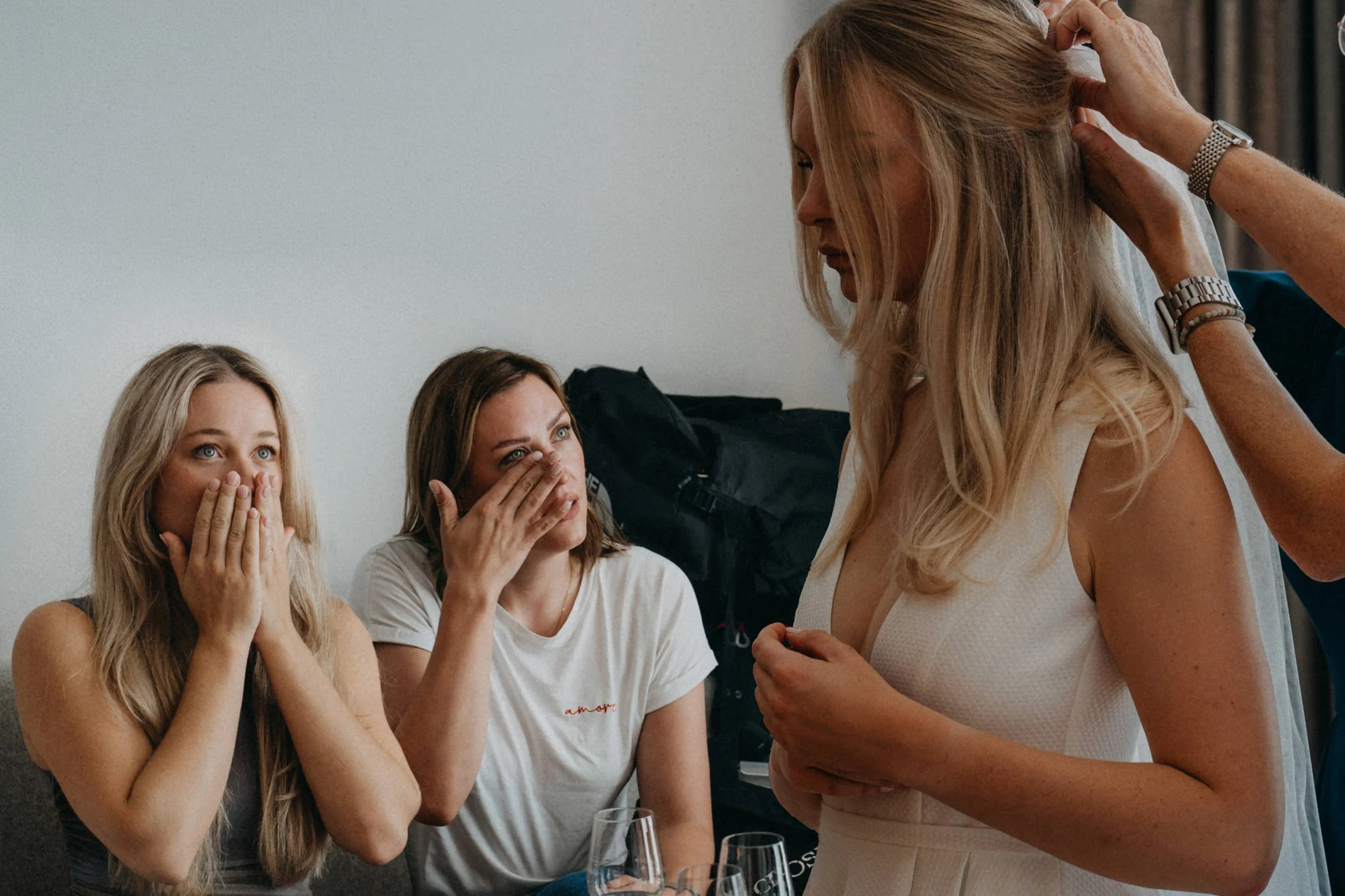 Drei Frauen reagieren überrascht und emotional, während eine andere Frau, vermutlich Friseurin, sie berührt und auf eine Veränderung vorbereitet.