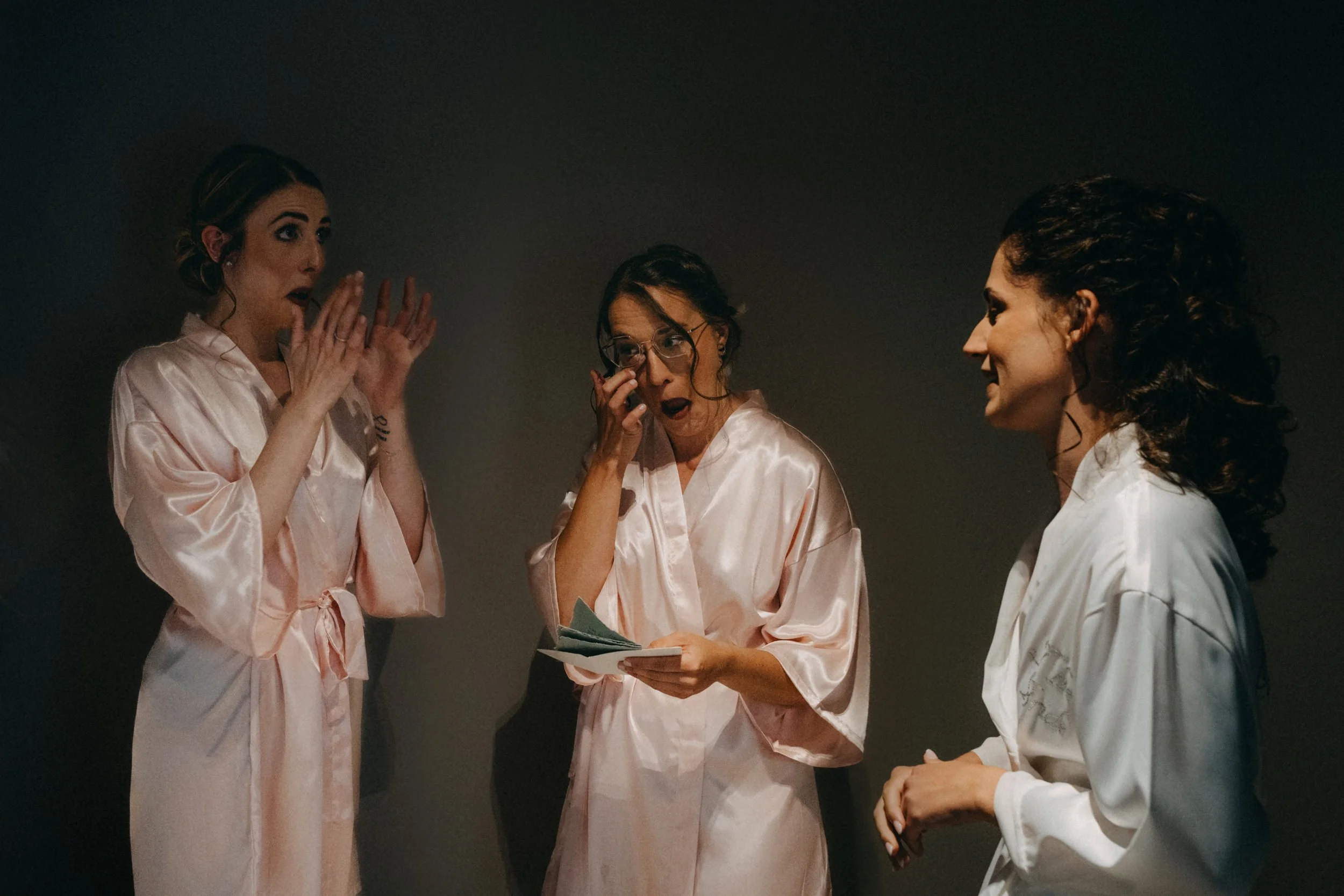 Drei Frauen in Satin-Pyjamas sprechen miteinander, eine der Frauen hält ein Telefon in der Hand.