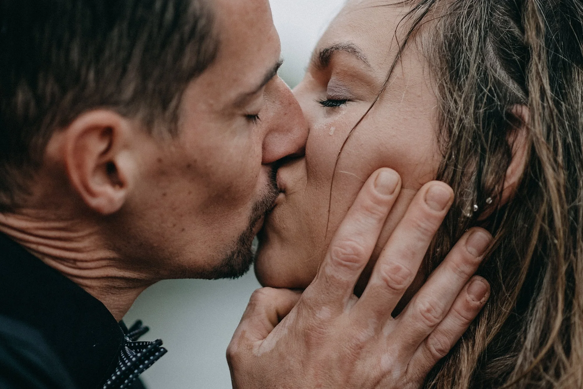 Ein Mann und eine Frau küssen sich leidenschaftlich, die Frau hält den Kopf des Mannes sanft mit beiden Händen, während sie ihre Augen geschlossen haben.