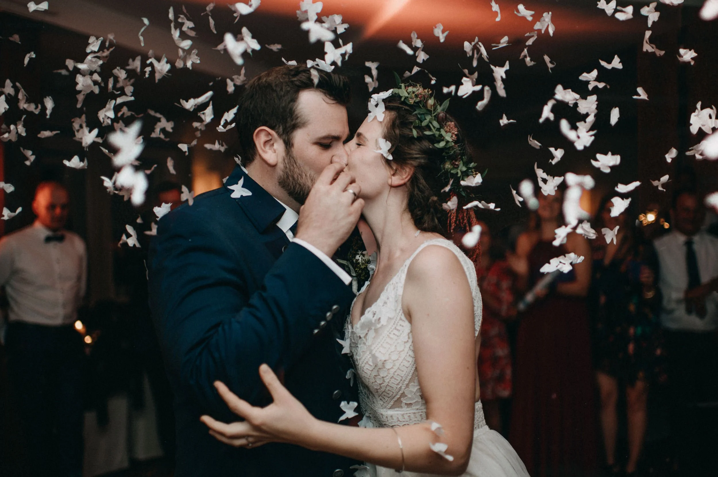 Ein Paar tanzt bei einer Hochzeit, umgeben von weißen Schmetterlingsdeko und Gästen im Hintergrund.
