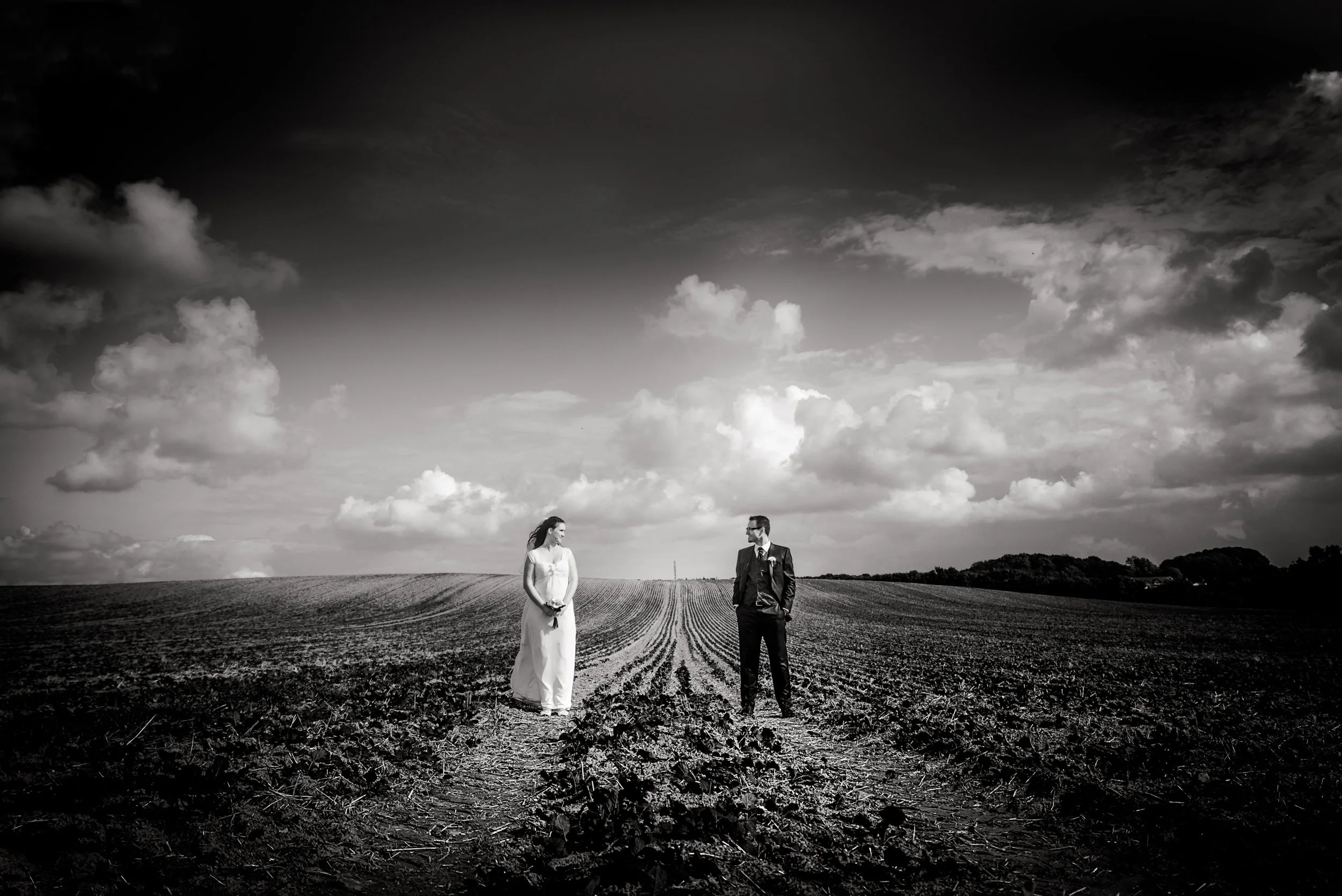 Ein Mann und eine Frau stehen auf einem Feld, im Hintergrund ein Himmel mit Wolken, schwarz-weiß Bild.