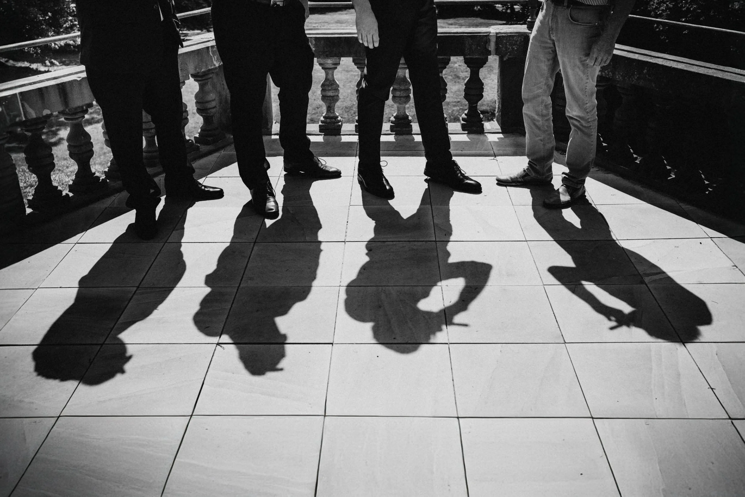 Schwarze und weiße Schatten von fünf Männern, die auf einem Balkon stehen, sichtbar, während die Sonne scheint.