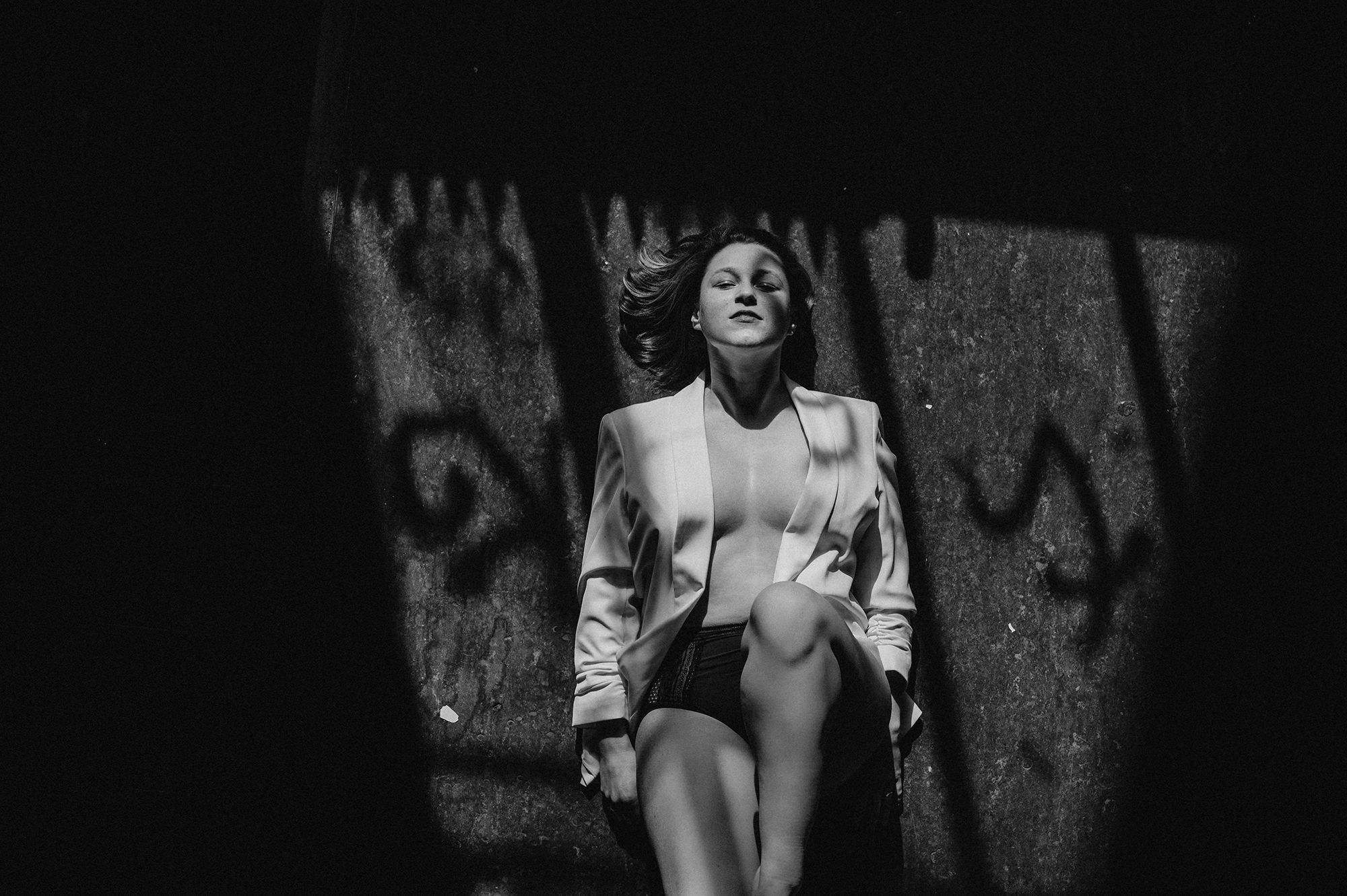 Schwarzweißfoto einer Frau, die auf dem Boden liegt, mit beleuchteten Schatten im Hintergrund.