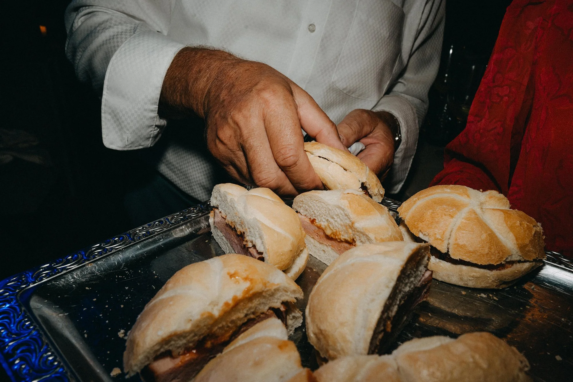 Nahaufnahme eines gedeckten Tisches mit Sandwiches, die auf einer glänzenden, silbernen Platte liegen. Die Sandwiches sind gefüllt mit Schinken und Käse, mit einem weichen Brötchen als obere Scheibe.