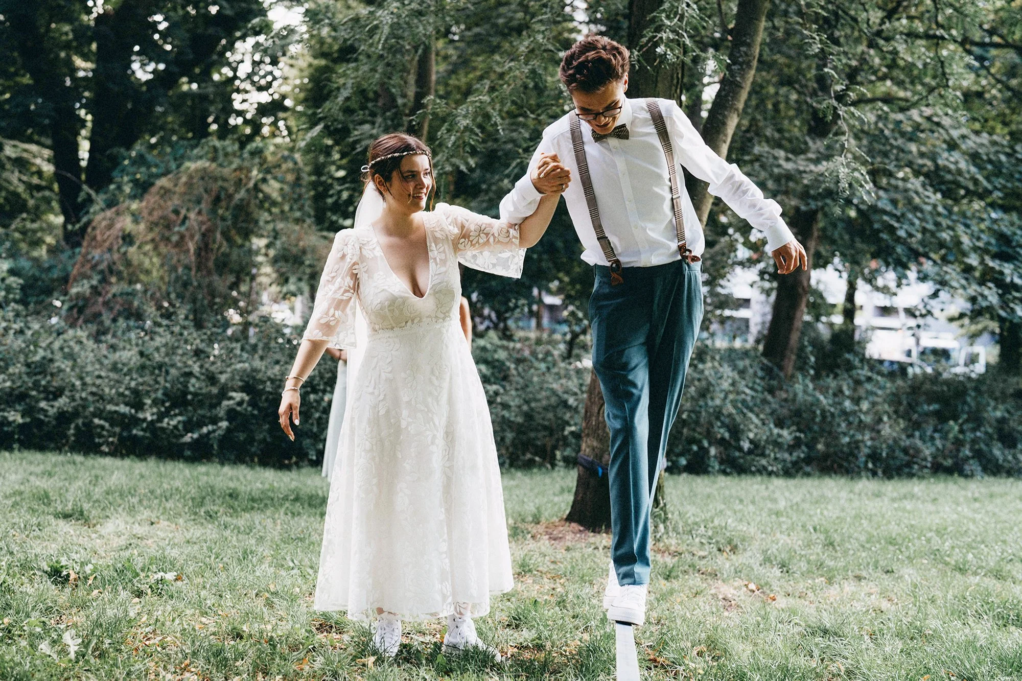 Ein Brautpaar tanzt im Park, die Braut trägt ein weißes Hochzeitskleid und der Bräutigam trägt Hemd, Weste, Hosenträger und eine Fliege.