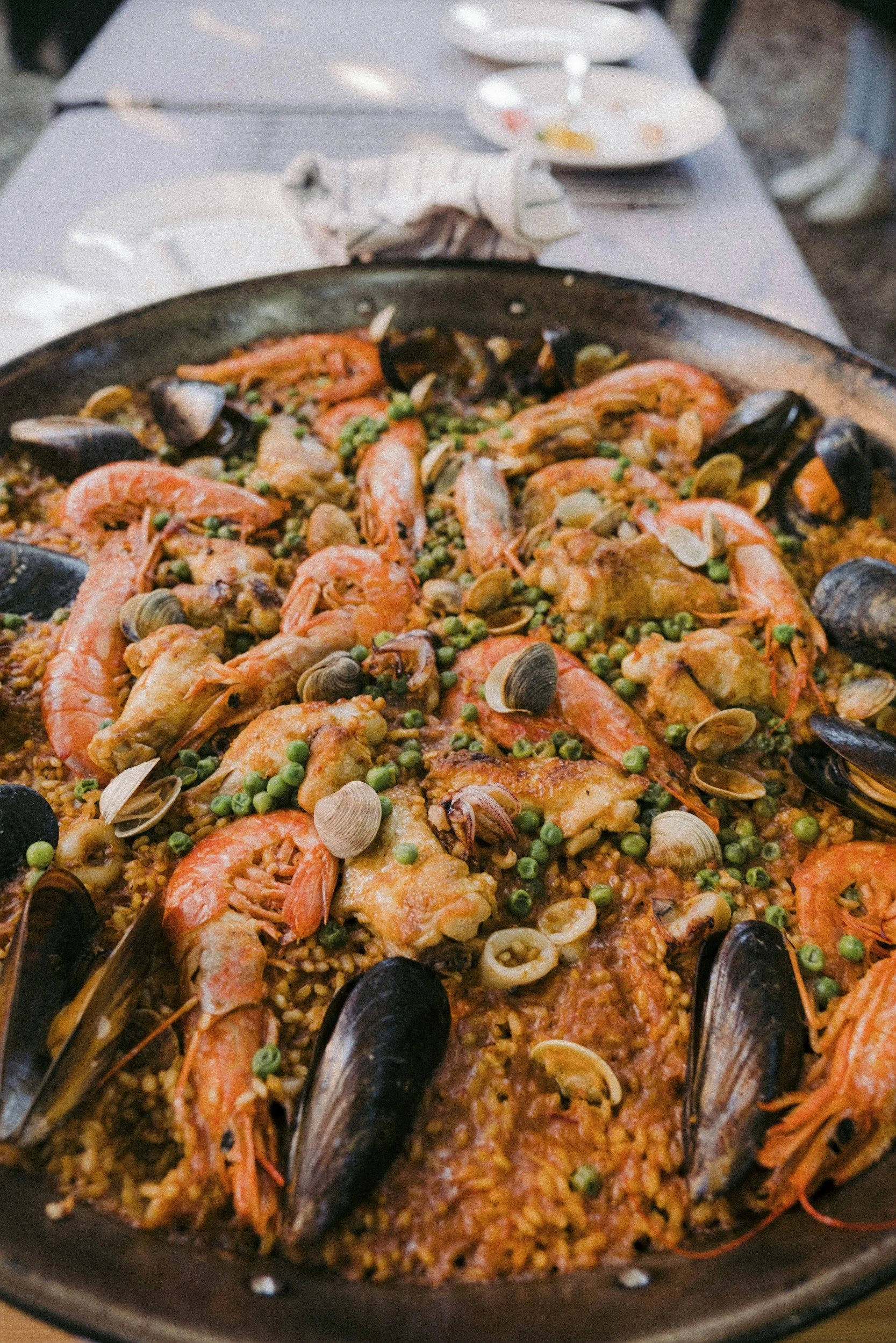 Seafood paella with shrimp, mussels, peas, and rice in a large pan.