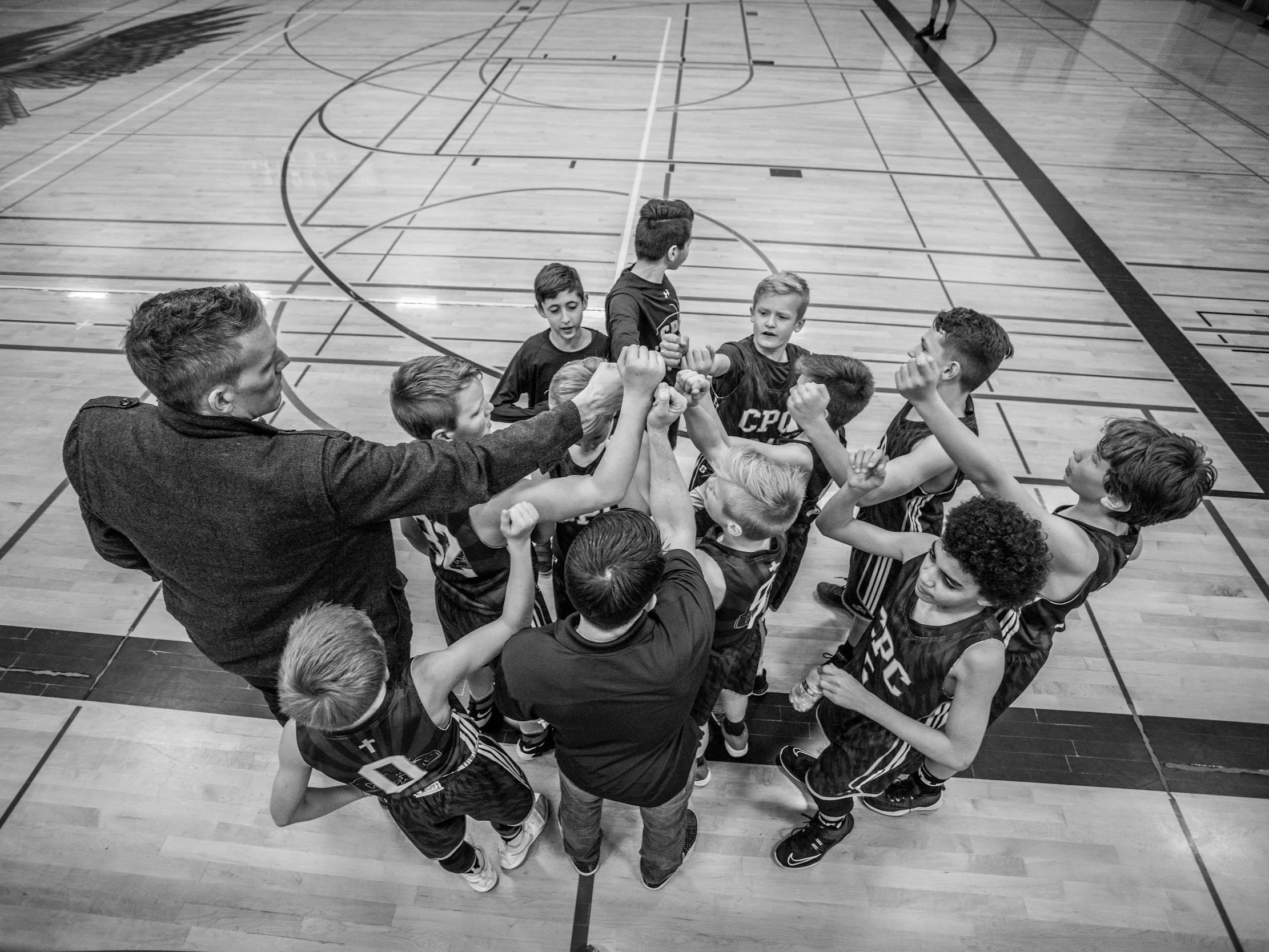 A basketball coach and a team of young players in a huddle on an indoor court.
