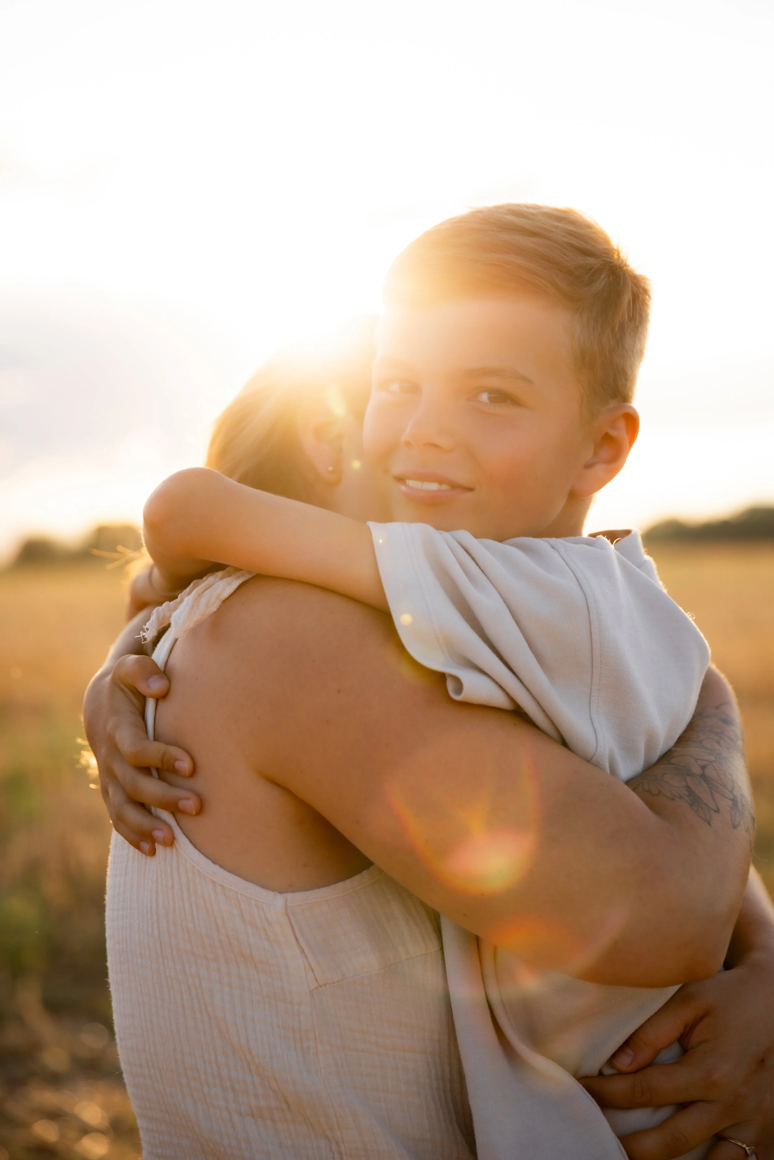 Un adolescent et une jeune fille se font un câlin dans un champ, en pleine lumière solaire, lors d'un coucher de soleil.