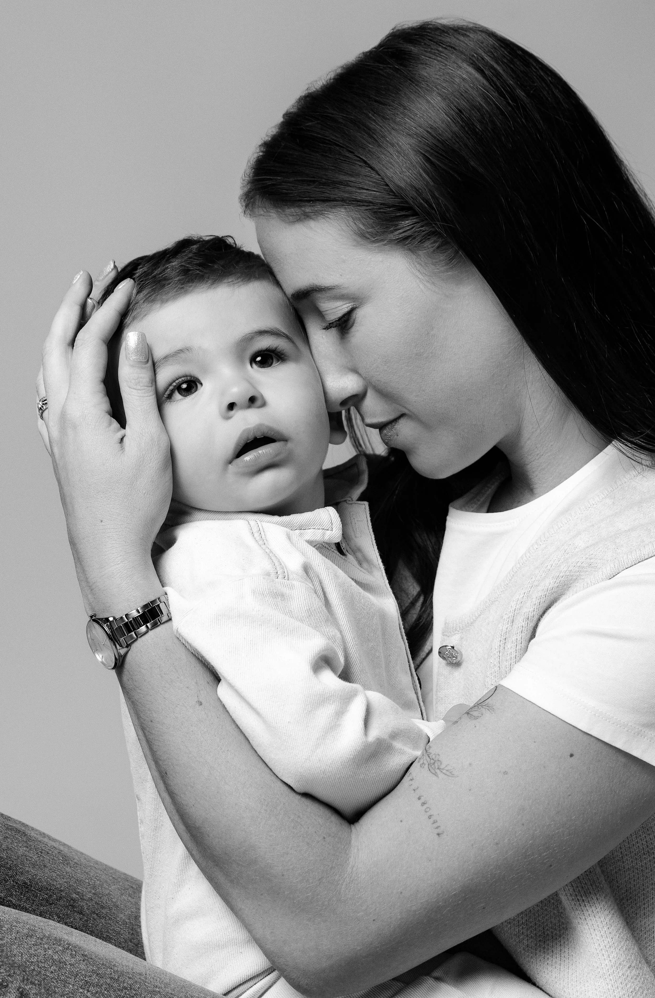 Une mère tient son jeune fils dans ses bras lors d'une séance photo en noir et blanc, exprimant tendresse et affection.