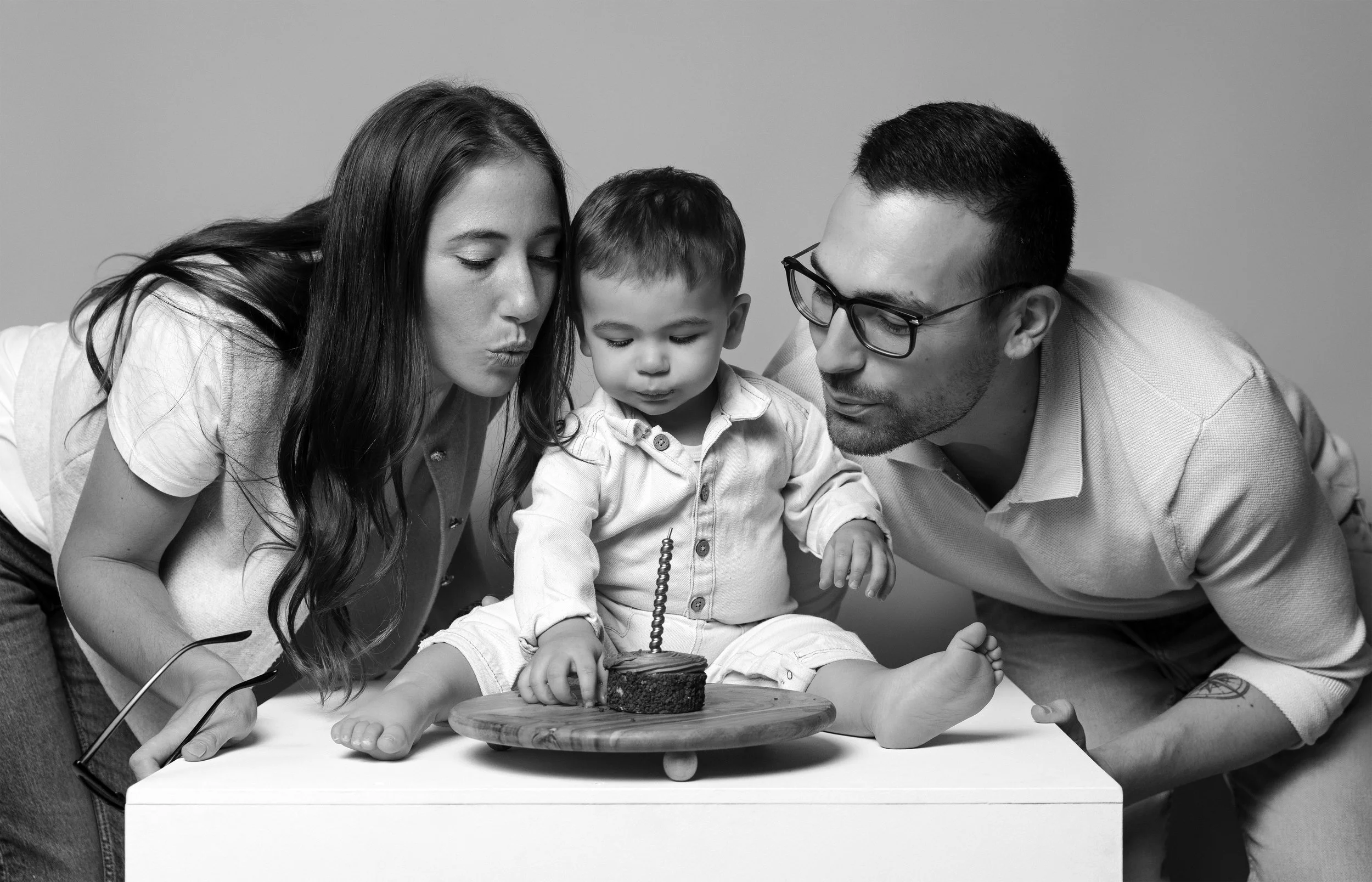 Une famille célèbre l'anniversaire d’un jeune garçon avec un gâteau. La mère à gauche, le père à droite, et l’enfant au centre, tous deux soufflant une bougie.