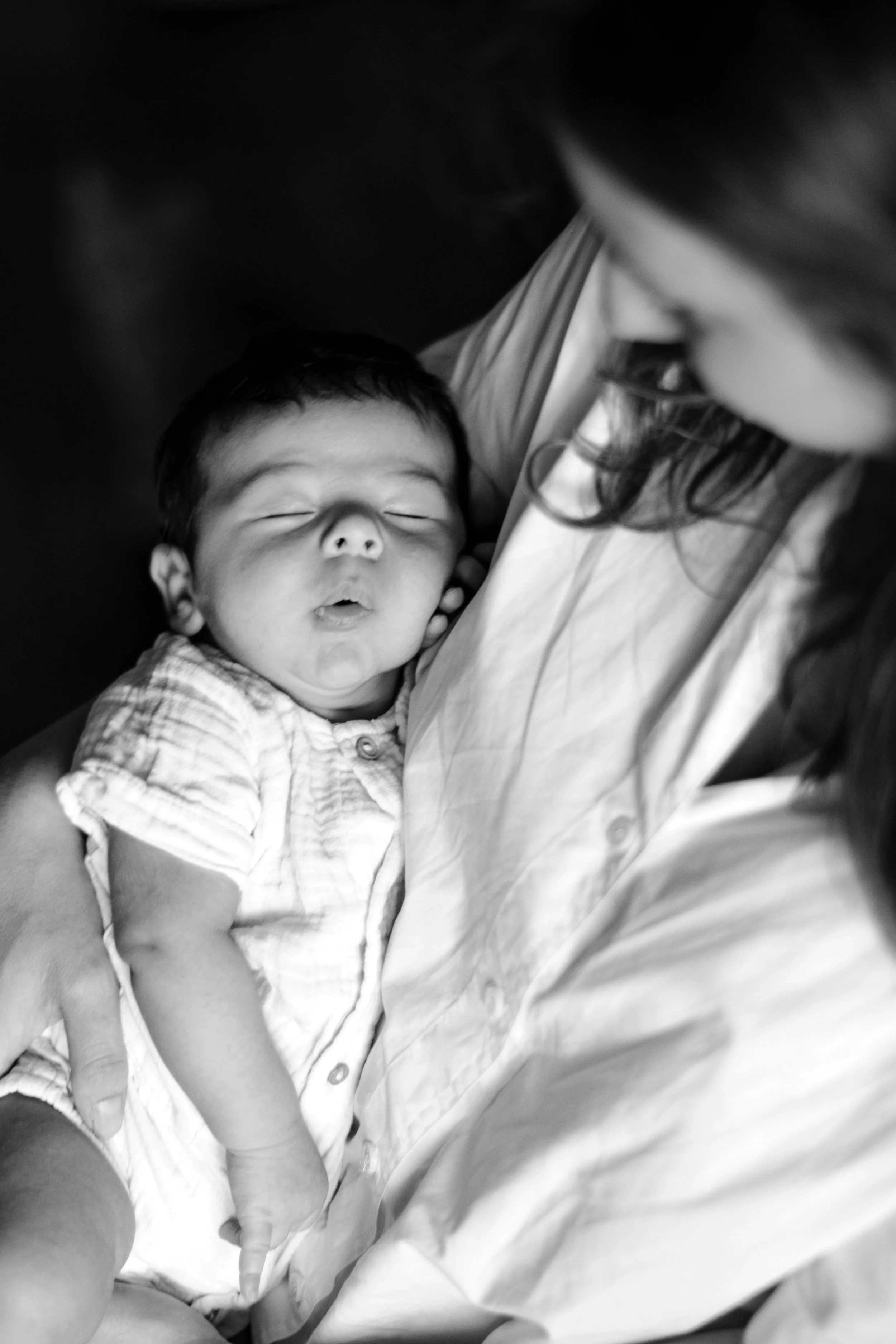 Une femme tient un bébé endormi contre elle, en noir et blanc.