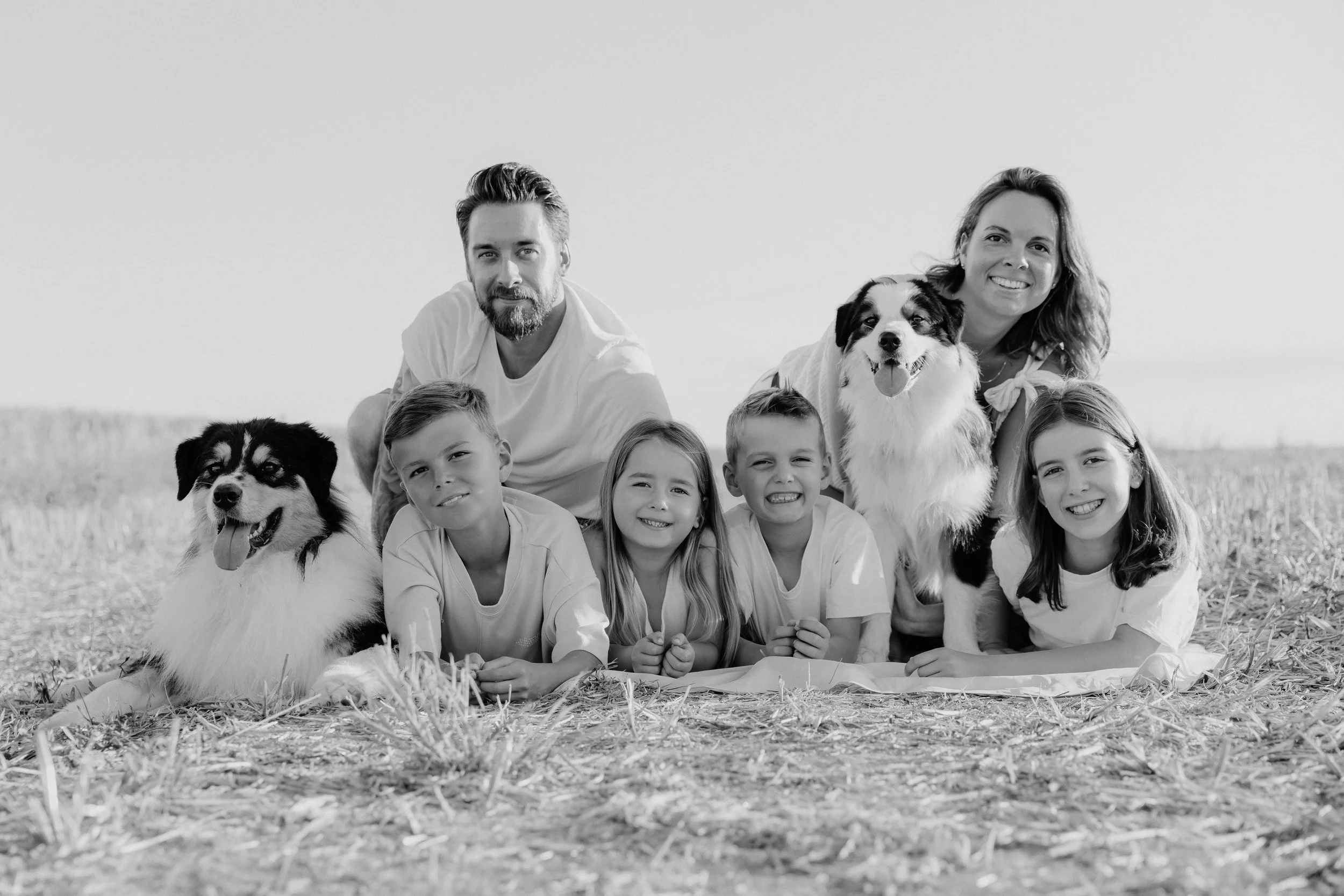 Une famille avec deux chiens, cinq enfants et deux adultes, posant sur un champ en plein air, souriants.