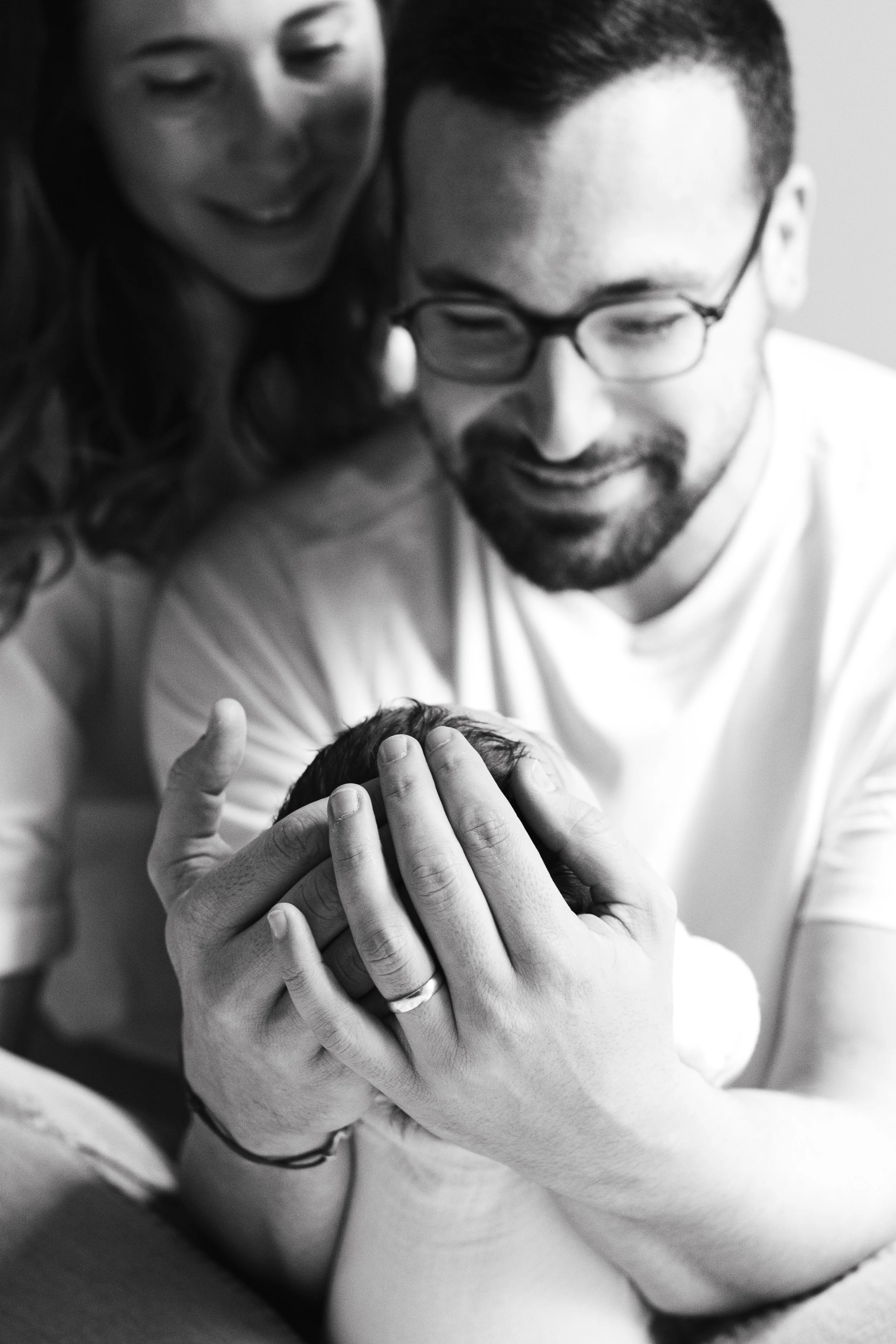 Une famille heureuse, avec un père et une mère regardant tendrement un nouveau-né, dans une photo en noir et blanc.