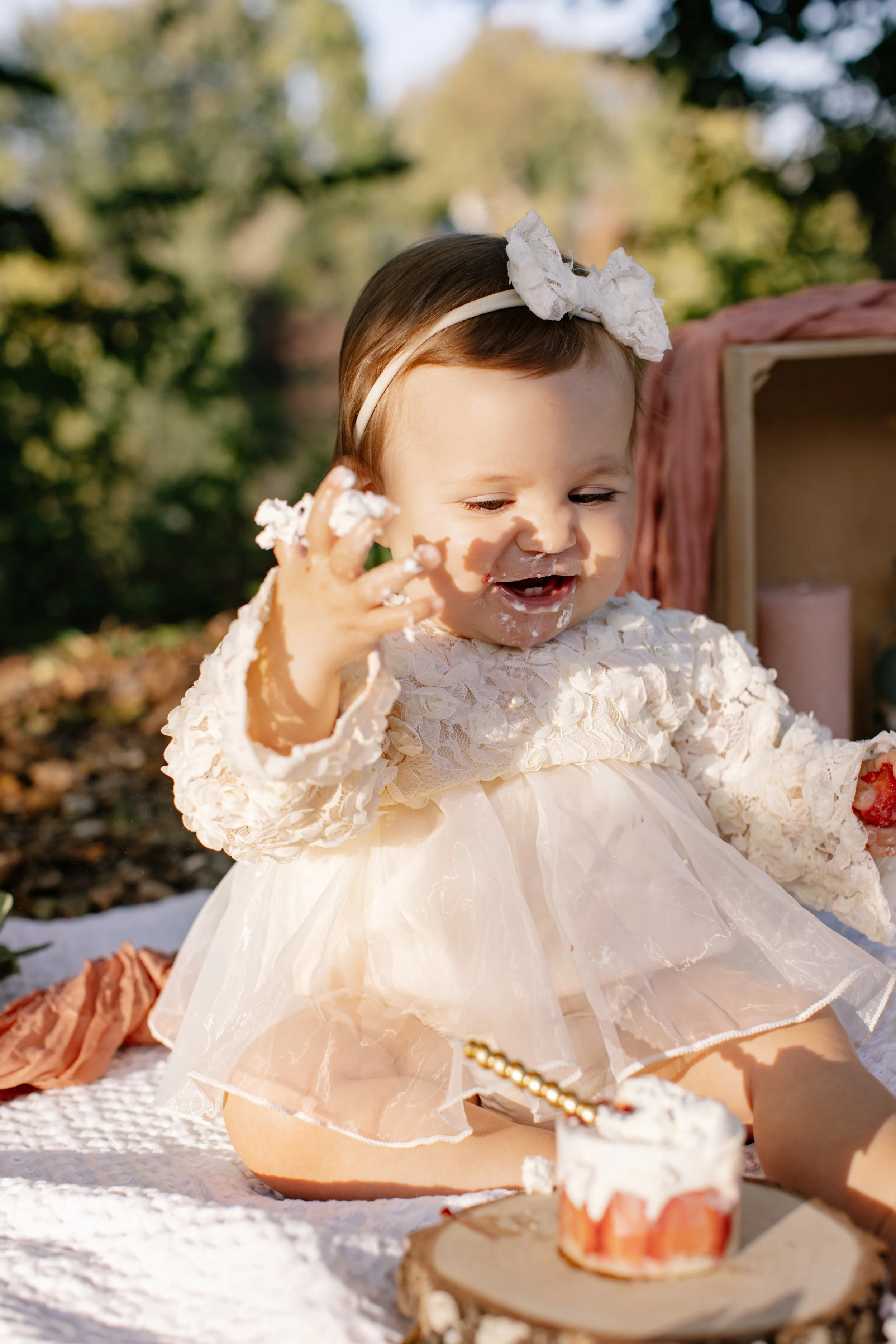 Jeune enfant en robe crème, faisant un gâteau d'anniversaire avec de la crème et des fraises, à l'extérieur lors d'une fête en plein air.